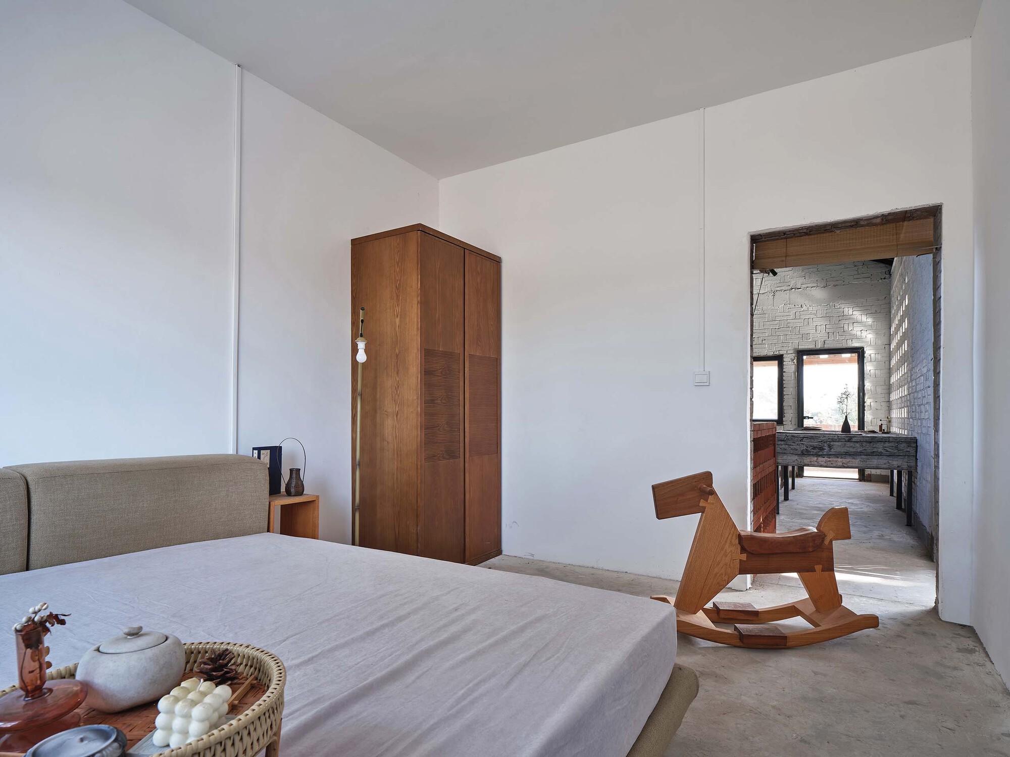 Bedroom with white walls and timber wardrobe looking through to an adjacent exposed brick space