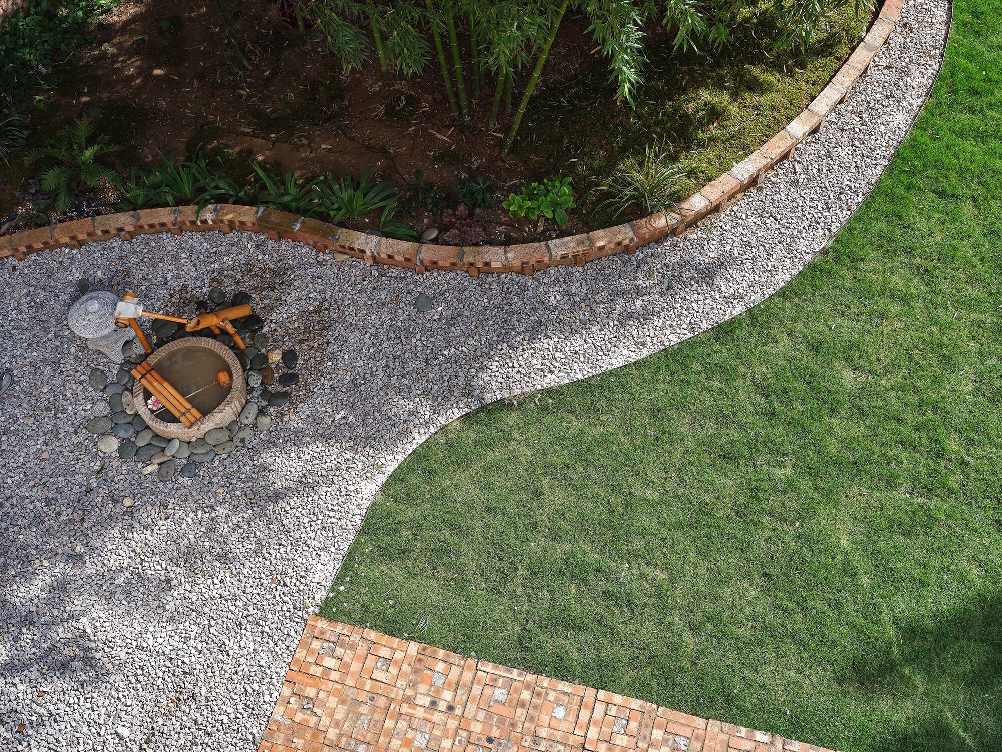 Aerial view of curved gravel pathways separating lawn and planted beds with bamboo and a central fire pit