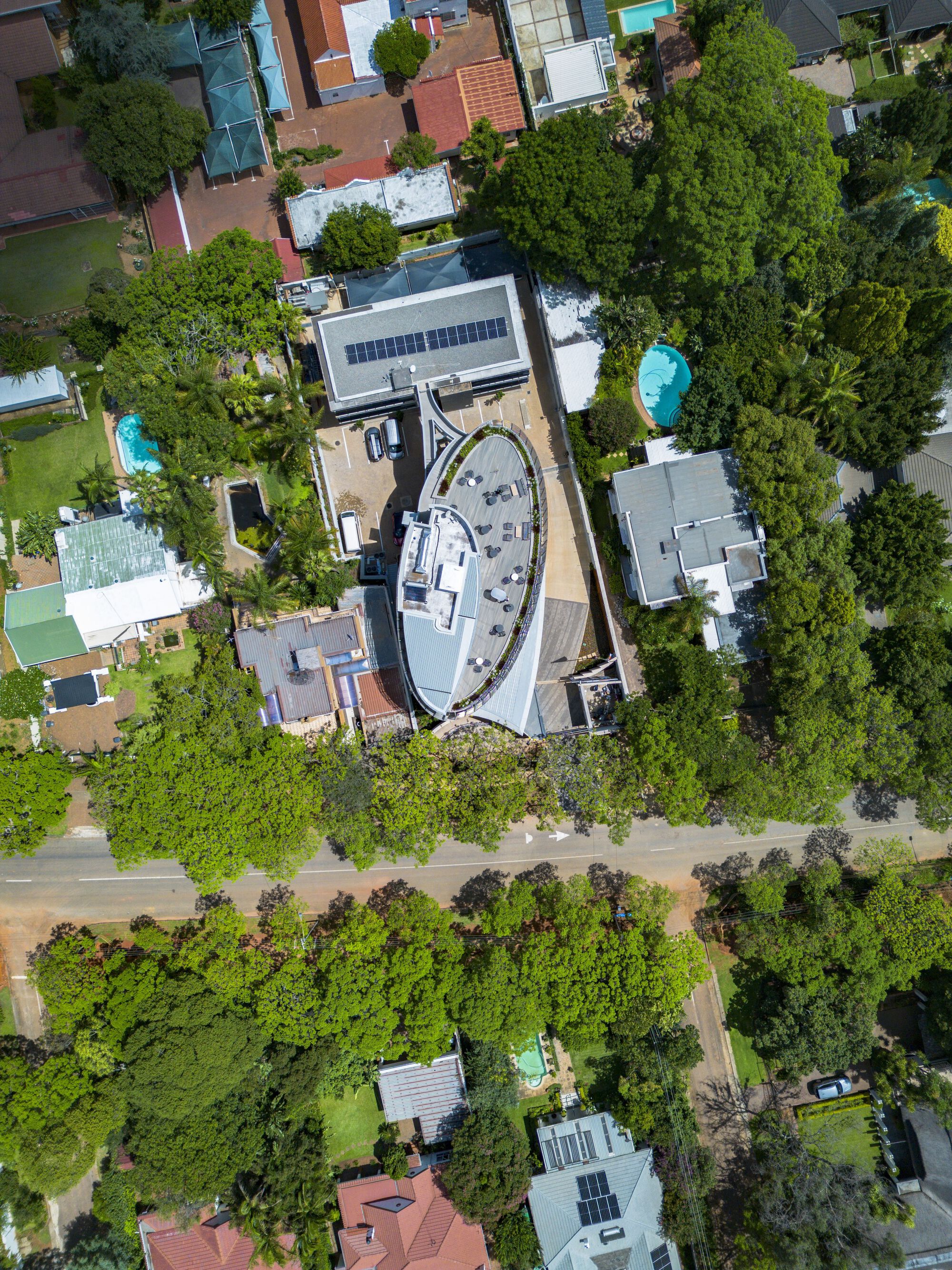 Drone view showing the oval rooftop terrace with solar panels and surrounding tree canopy