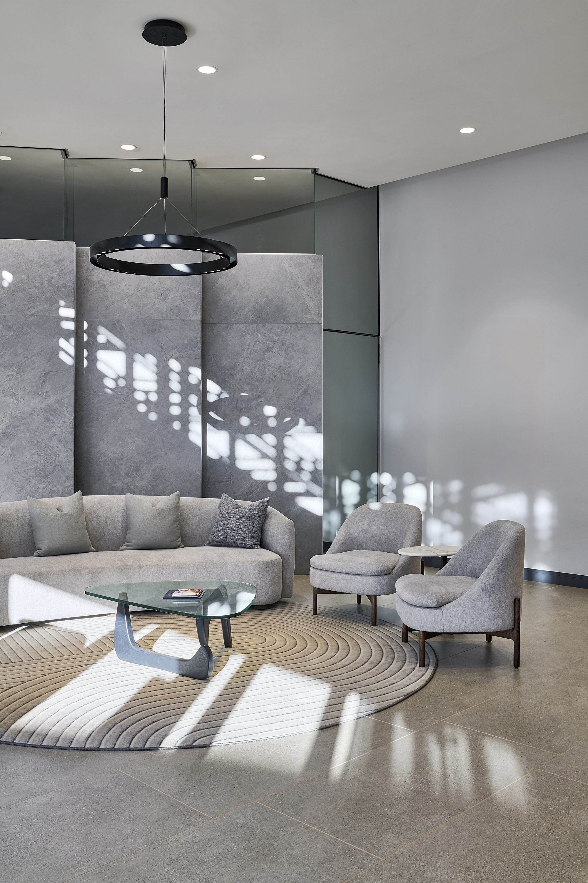 Double-height lounge with filtered light casting geometric shadows across concrete panels and polished floor