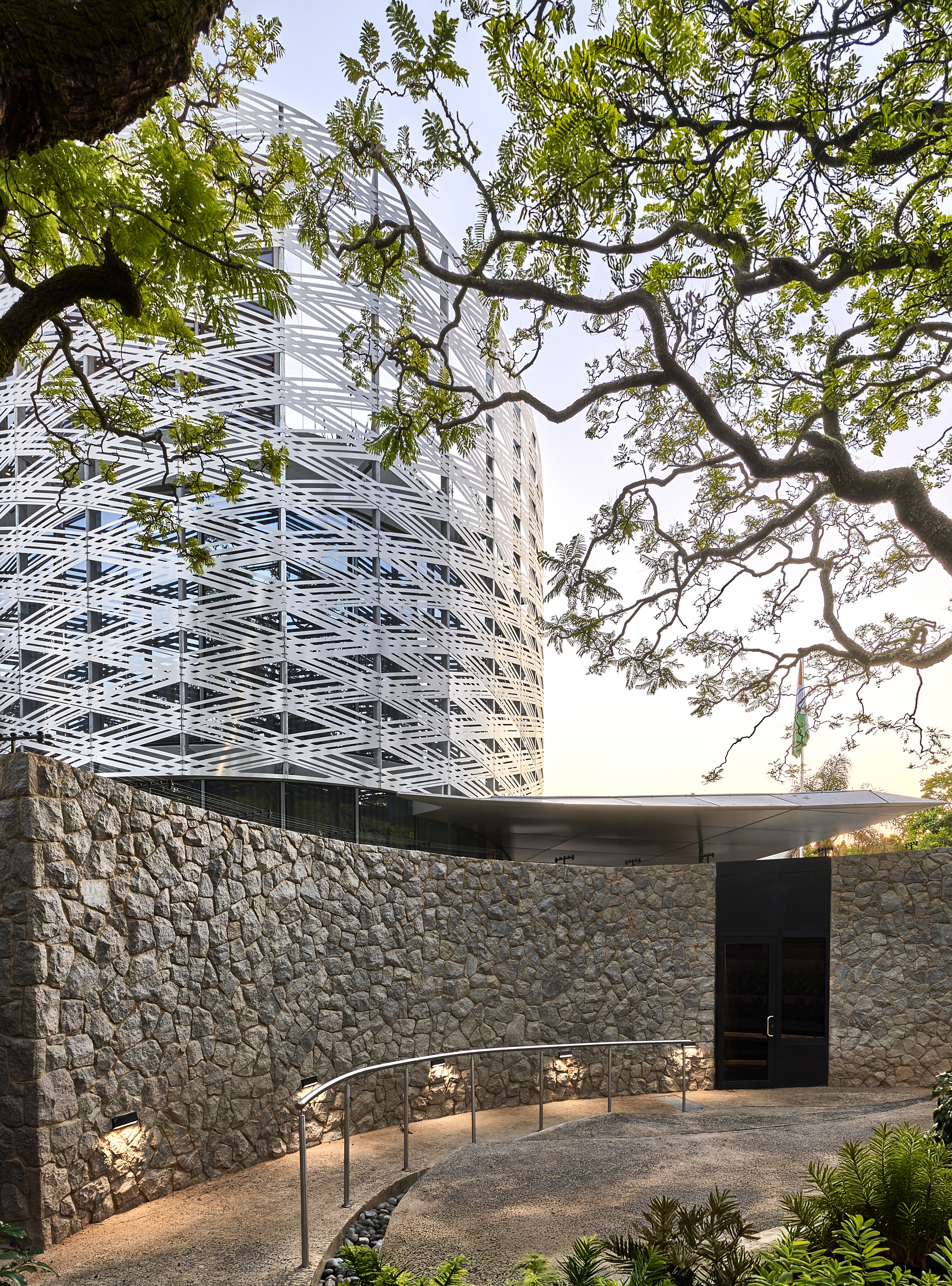 Entry courtyard with stone retaining wall and overhanging tree branch framing the white screen facade