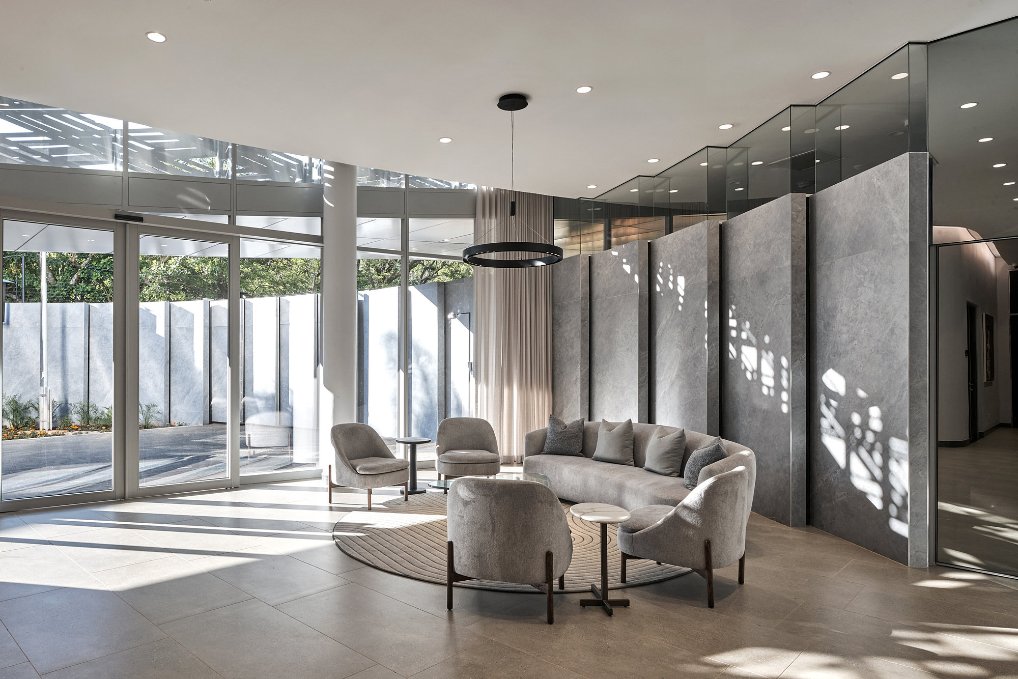 Interior seating area with floor-to-ceiling glazing overlooking courtyard and patterned light on concrete walls
