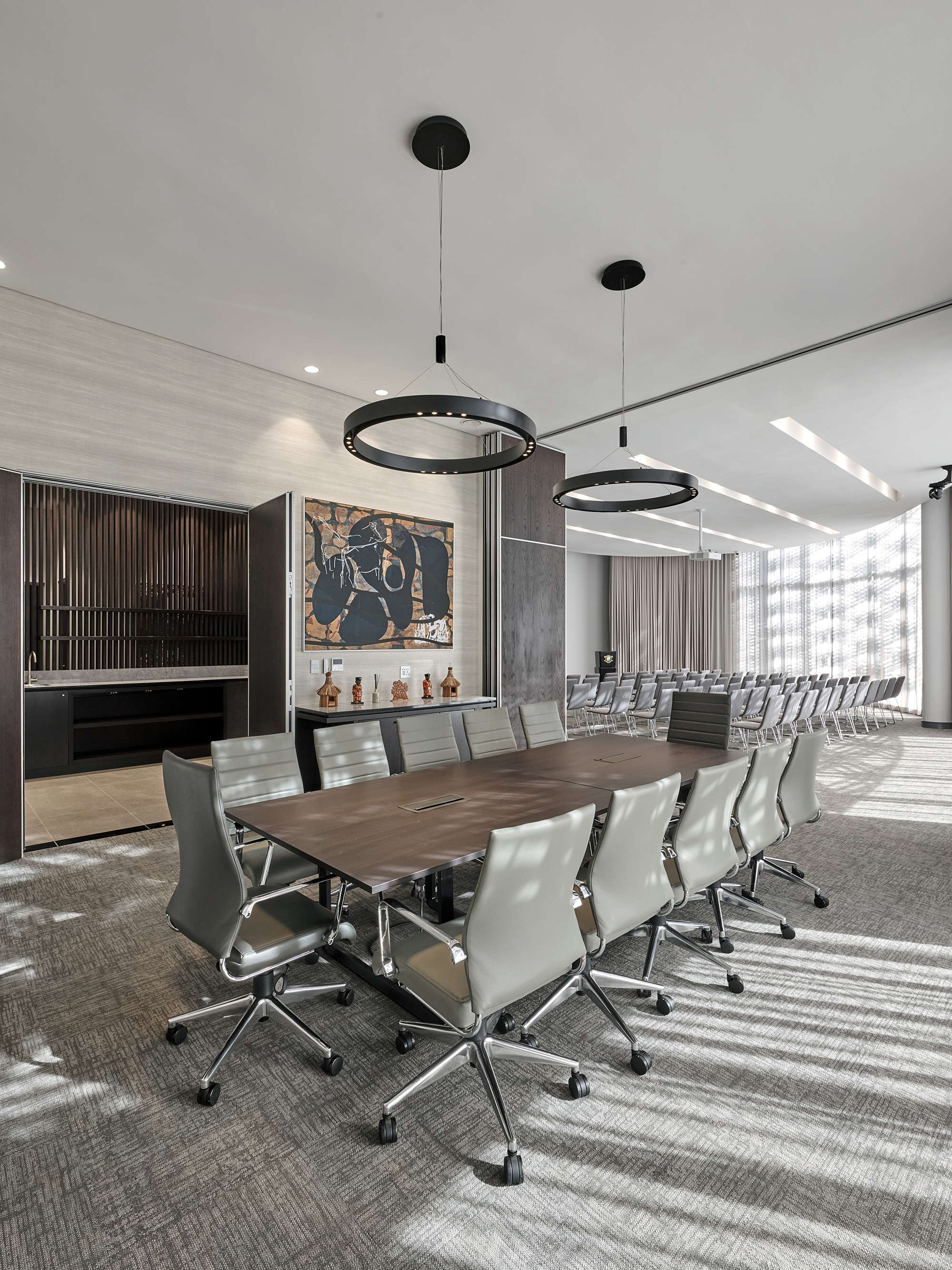 Conference room with long wooden table and white leather chairs beneath black circular pendant lights
