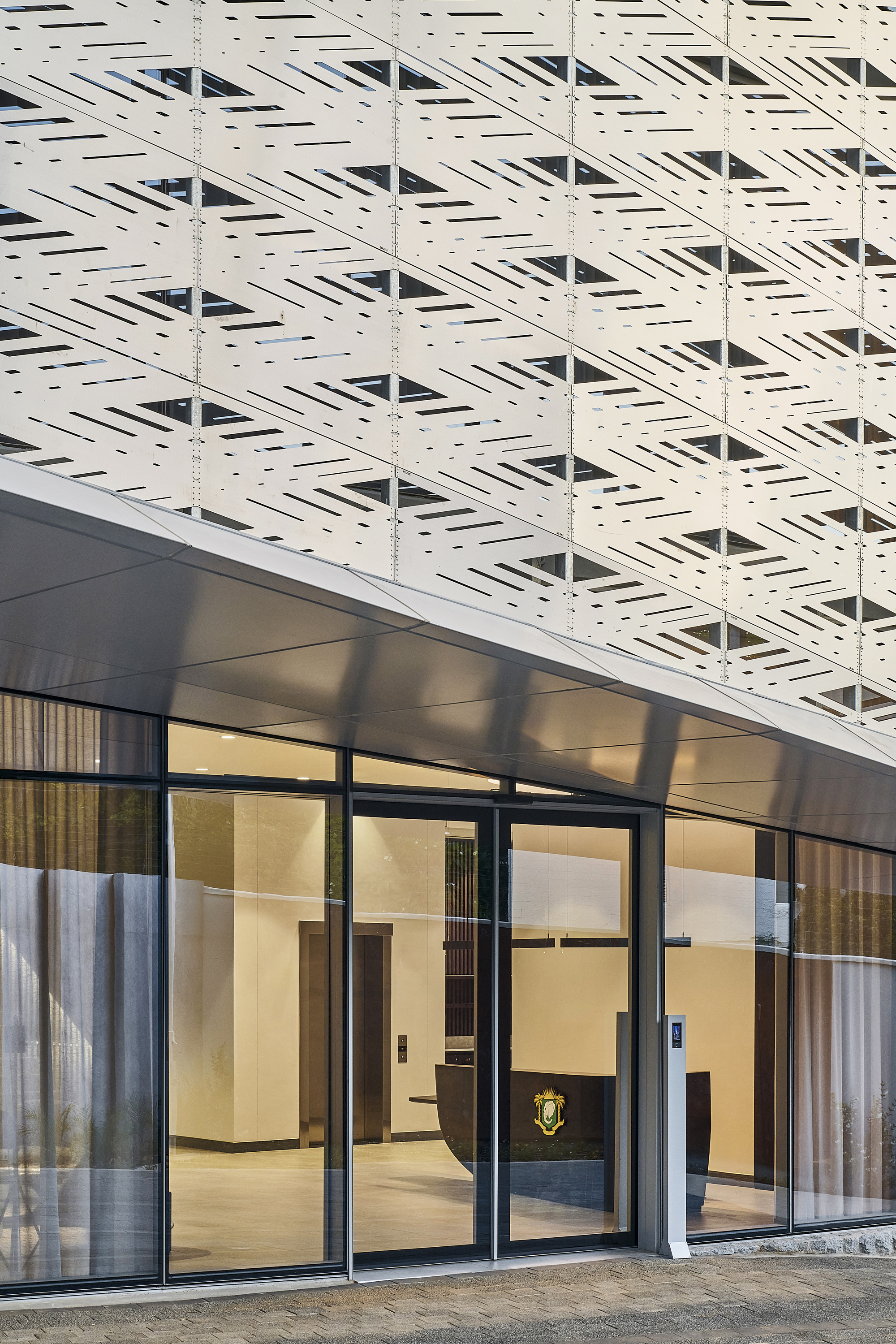 Ground floor entrance with black framed glazing beneath a white perforated panel facade at dusk