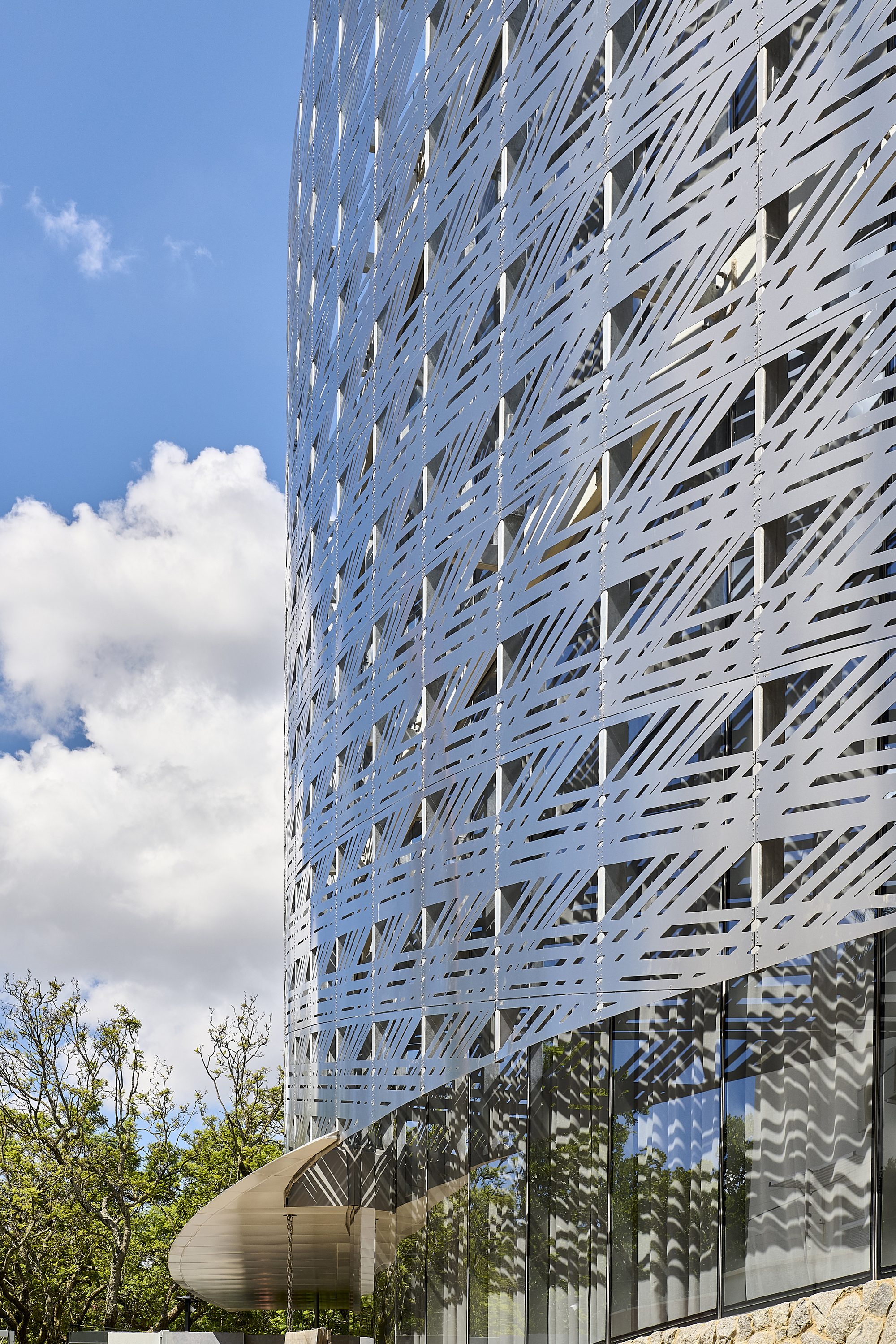 Perforated white metal screen wrapping the tower facade with clouds reflected in the glazing below