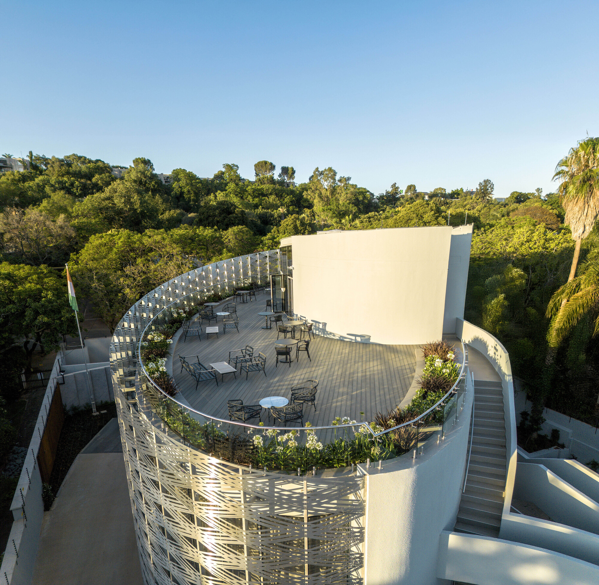 Aerial view of curved rooftop terrace with outdoor furniture and planted beds in late afternoon light