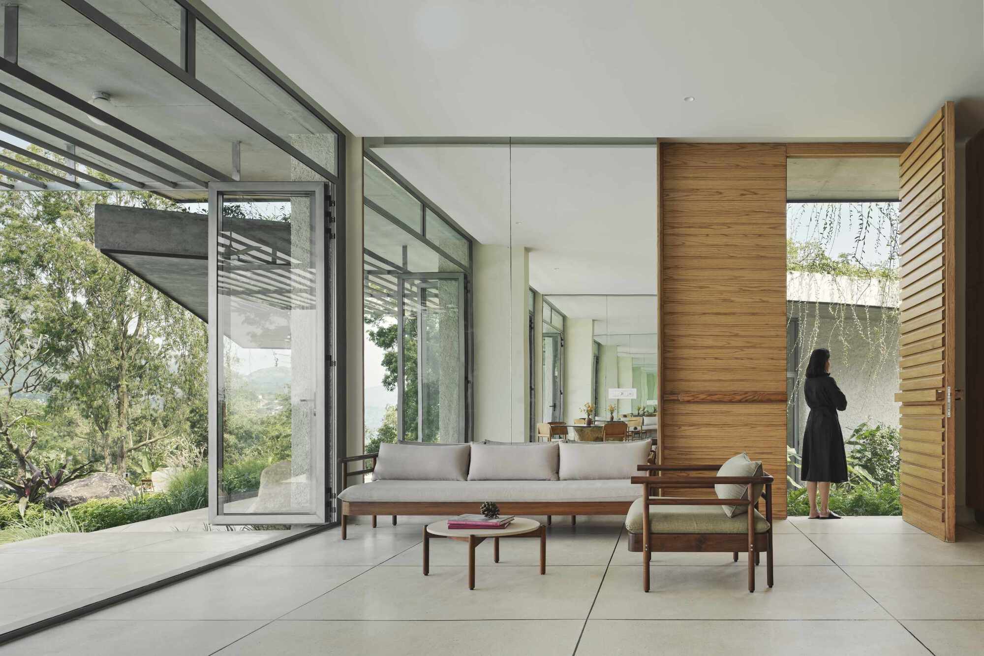 Open living space with folding glass walls, timber feature wall, and a figure standing by the courtyard