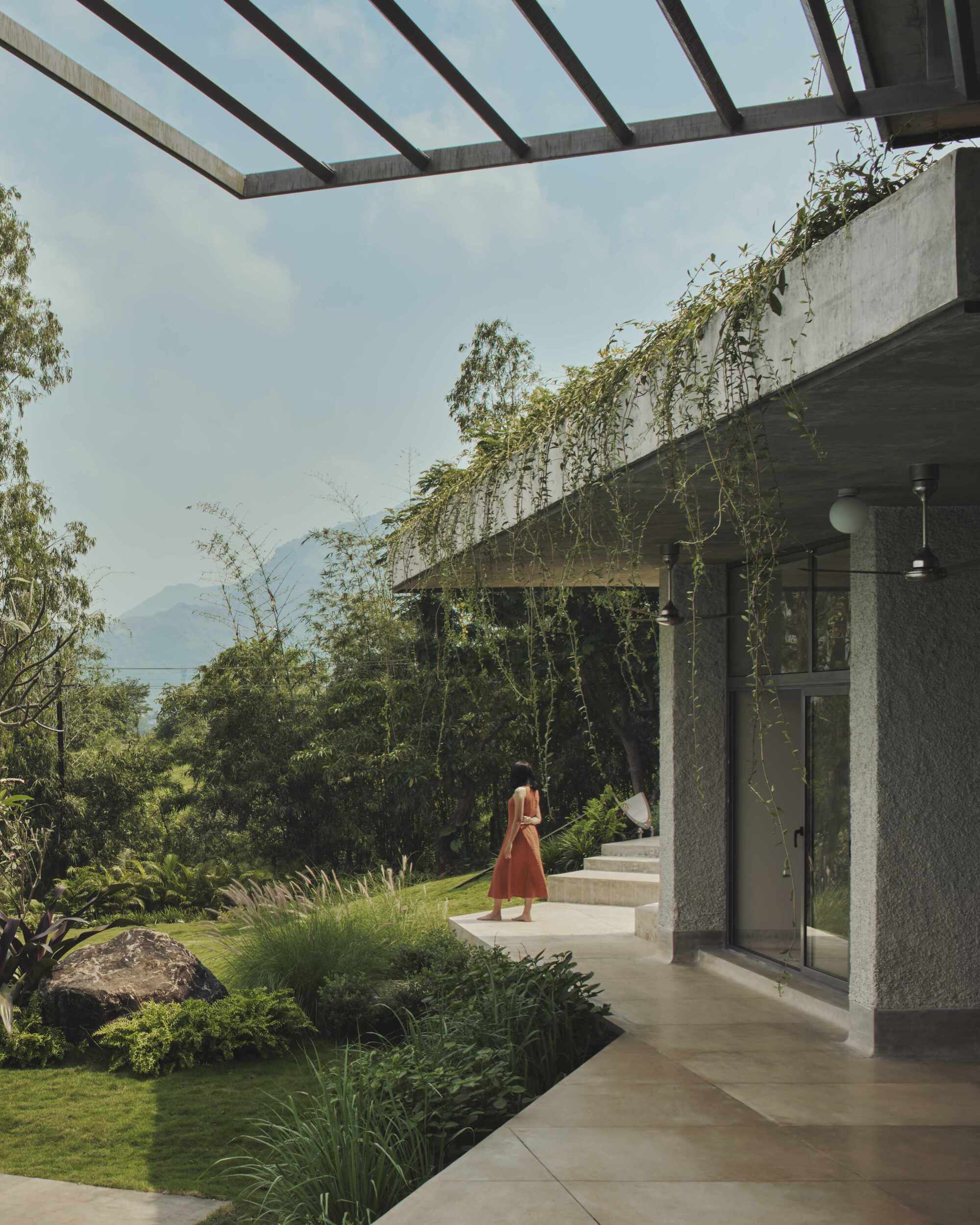 Covered walkway with concrete pergola beams and planted roof edges framing a view toward distant mountains
