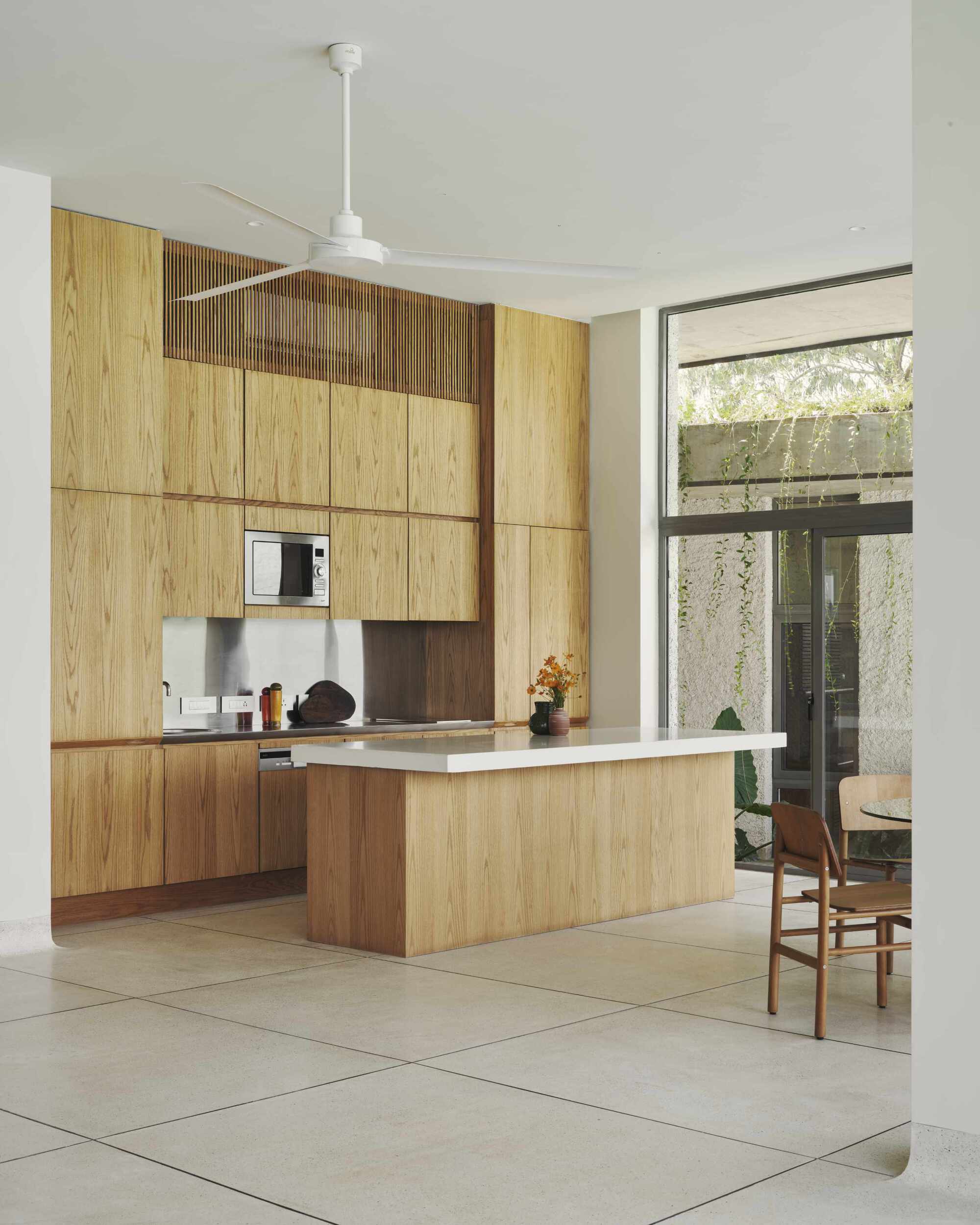 Open kitchen with oak island and cabinetry opening to planted courtyard through glazed corner doors
