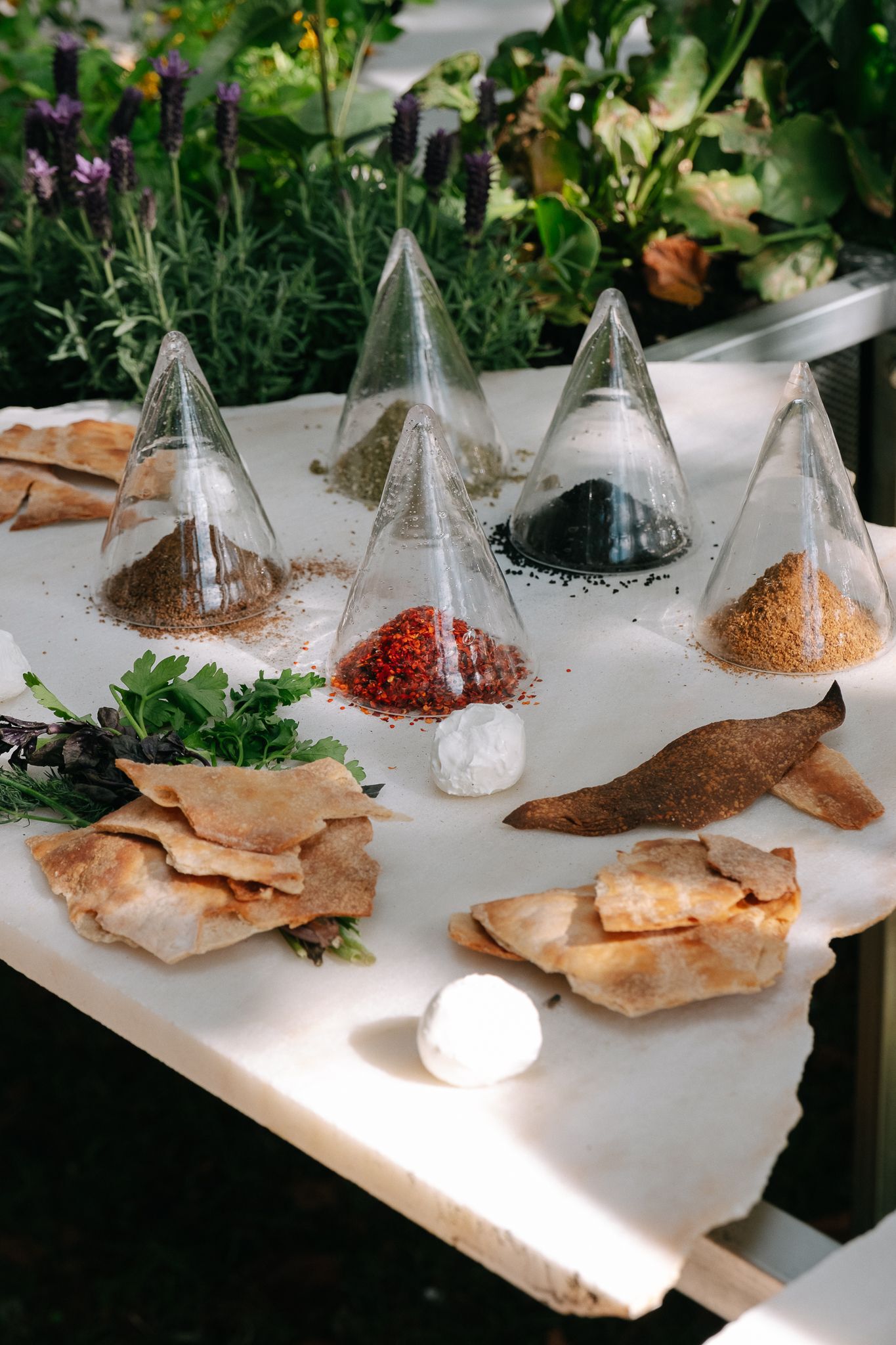Tabletop display of glass pyramid vessels filled with colored spices and dried herbs