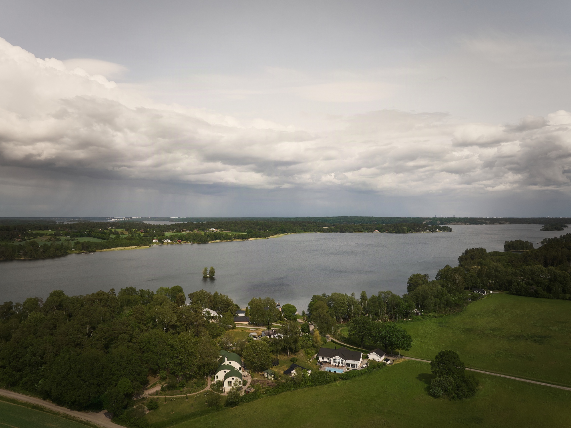 Aerial view of the cluster of barrel-roofed structures nestled among trees beside a lake under storm clouds