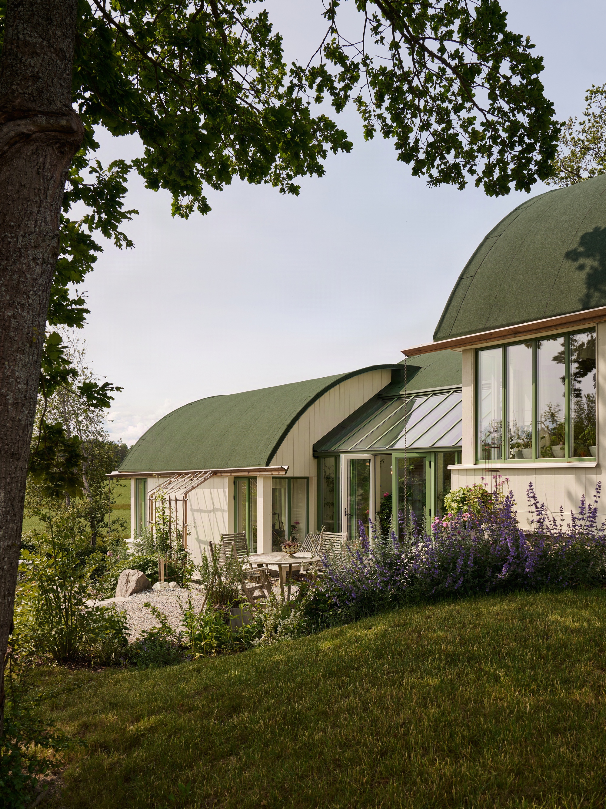 Corner terrace with glazed walls beneath the overhanging green barrel roof and oak tree canopy overhead