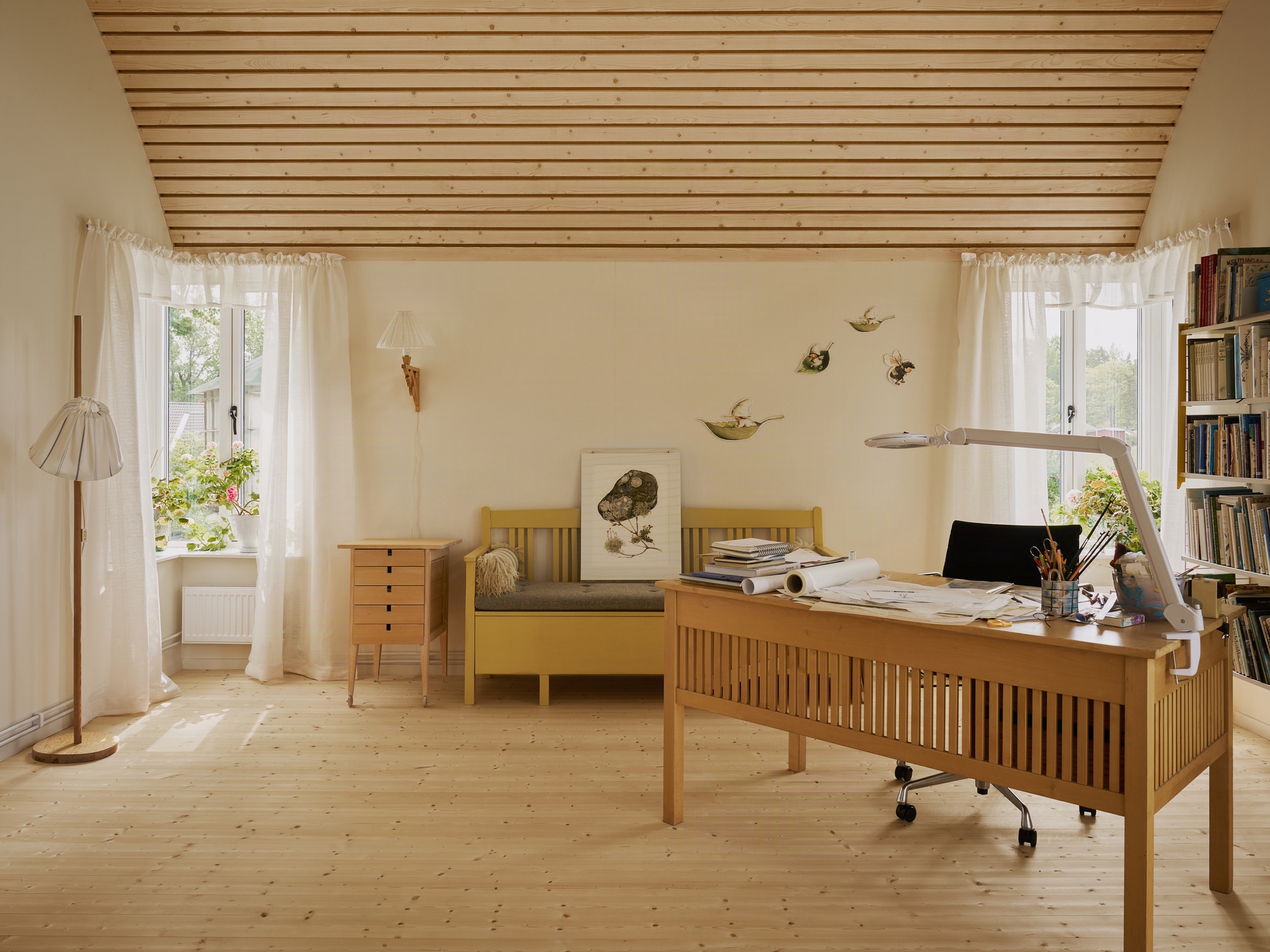 Home office with wooden desk and slatted ceiling panel beneath two curtained windows