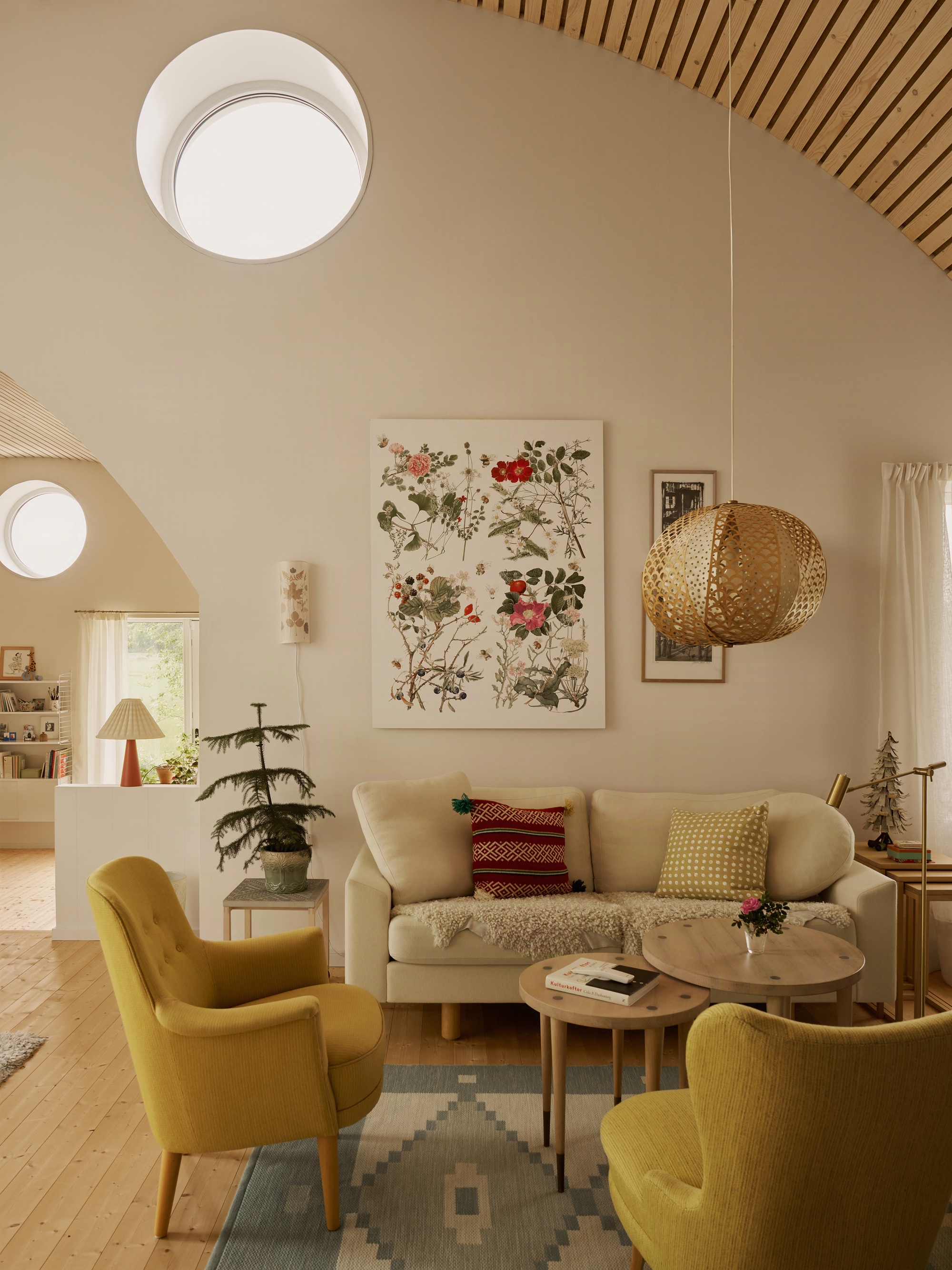 Living room with circular skylights, timber slatted ceiling and floral tapestry above a cream sofa