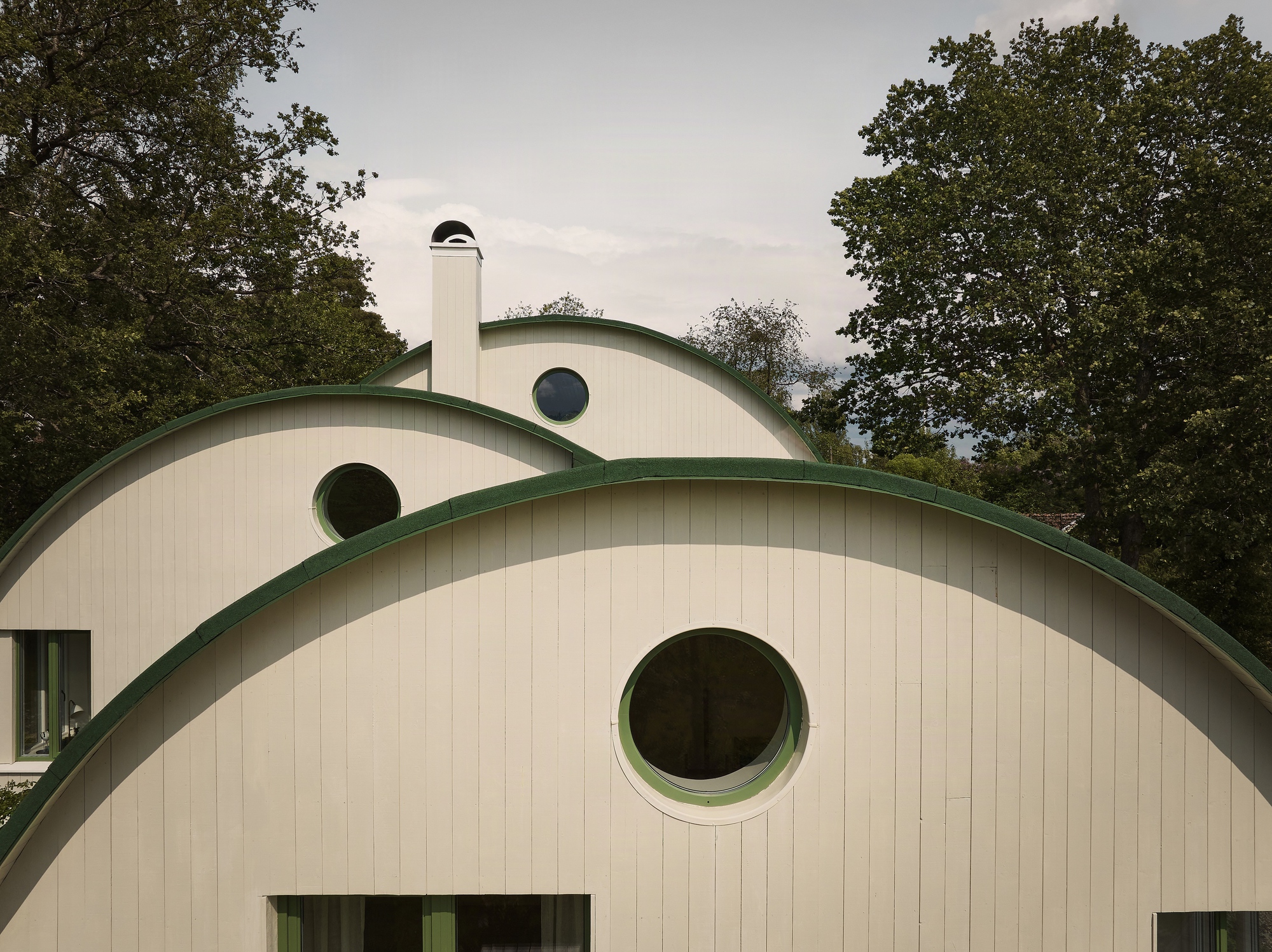 Arched facades with vertical paneling and green trim punctuated by circular windows beneath an overcast sky