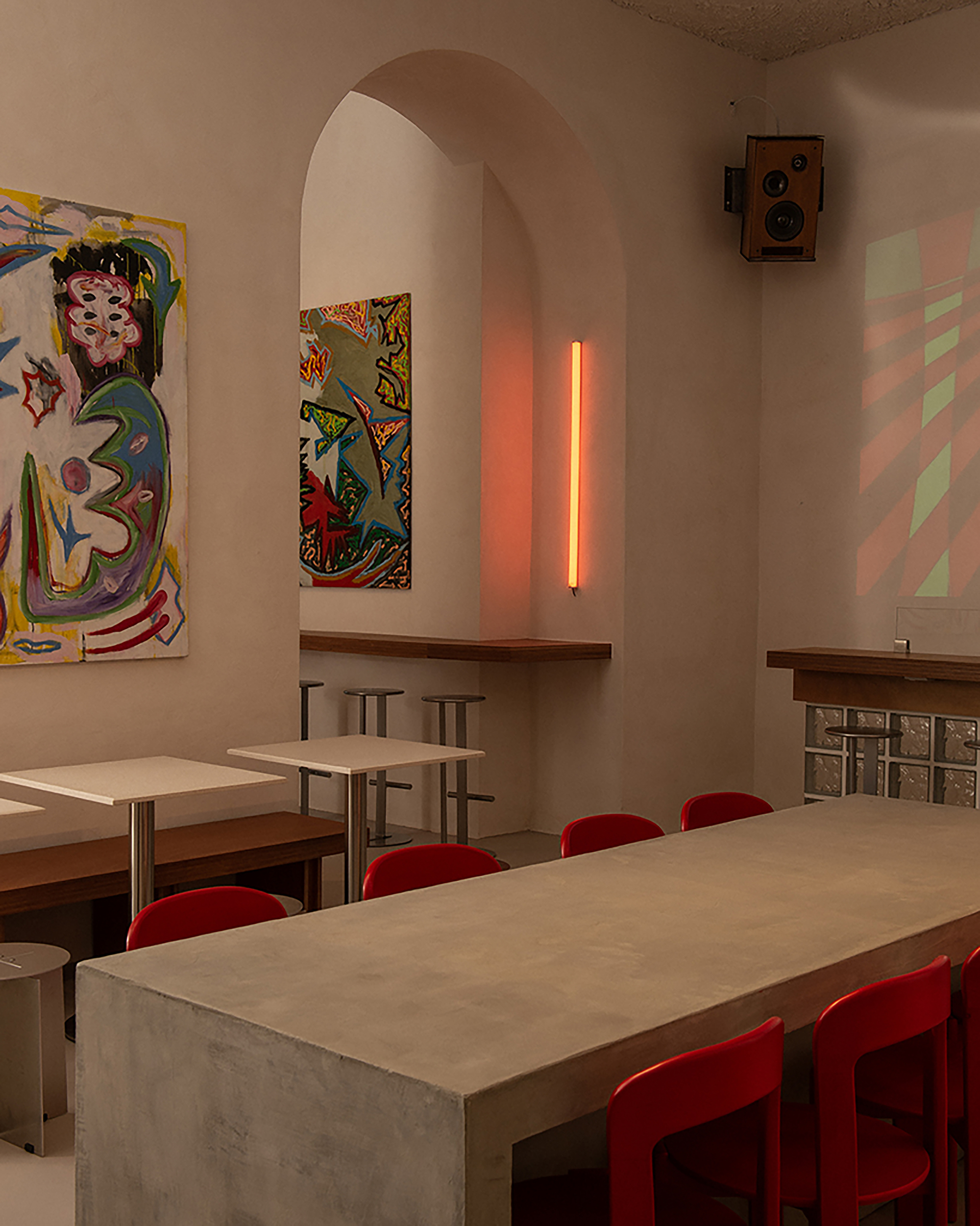 Dining table with red chairs beneath arched alcove with orange tube light and colorful paintings