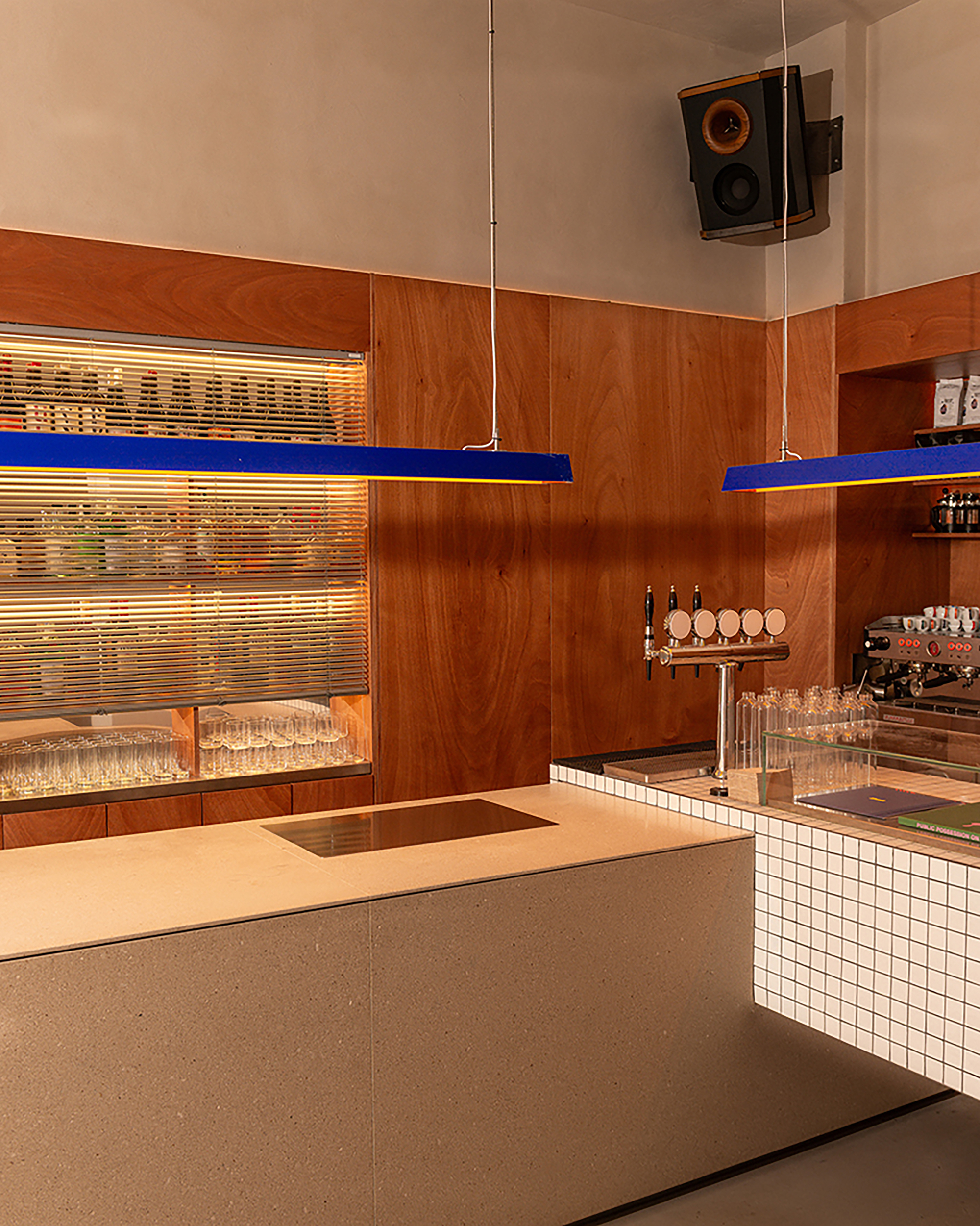 Service bar with terrazzo counter, white tile front, timber cabinetry, beer taps and suspended blue light fixture
