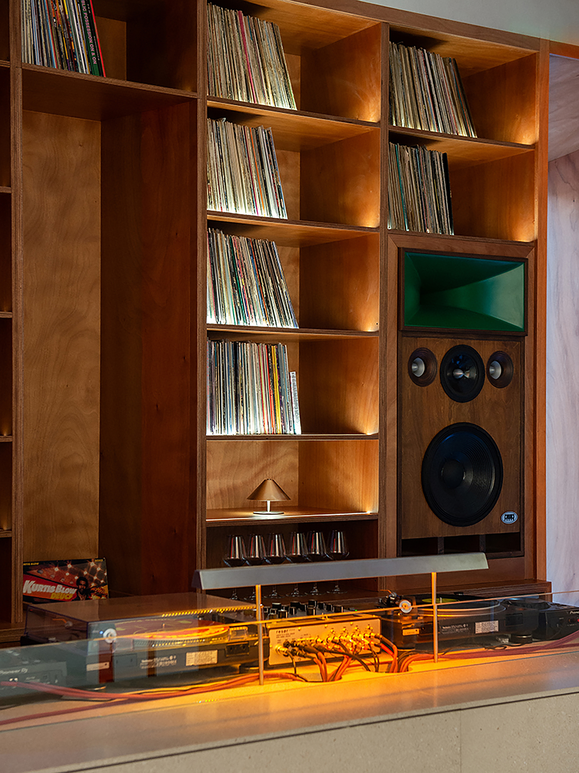 Timber shelving unit holding vinyl records with integrated speakers and audio equipment under yellow lighting