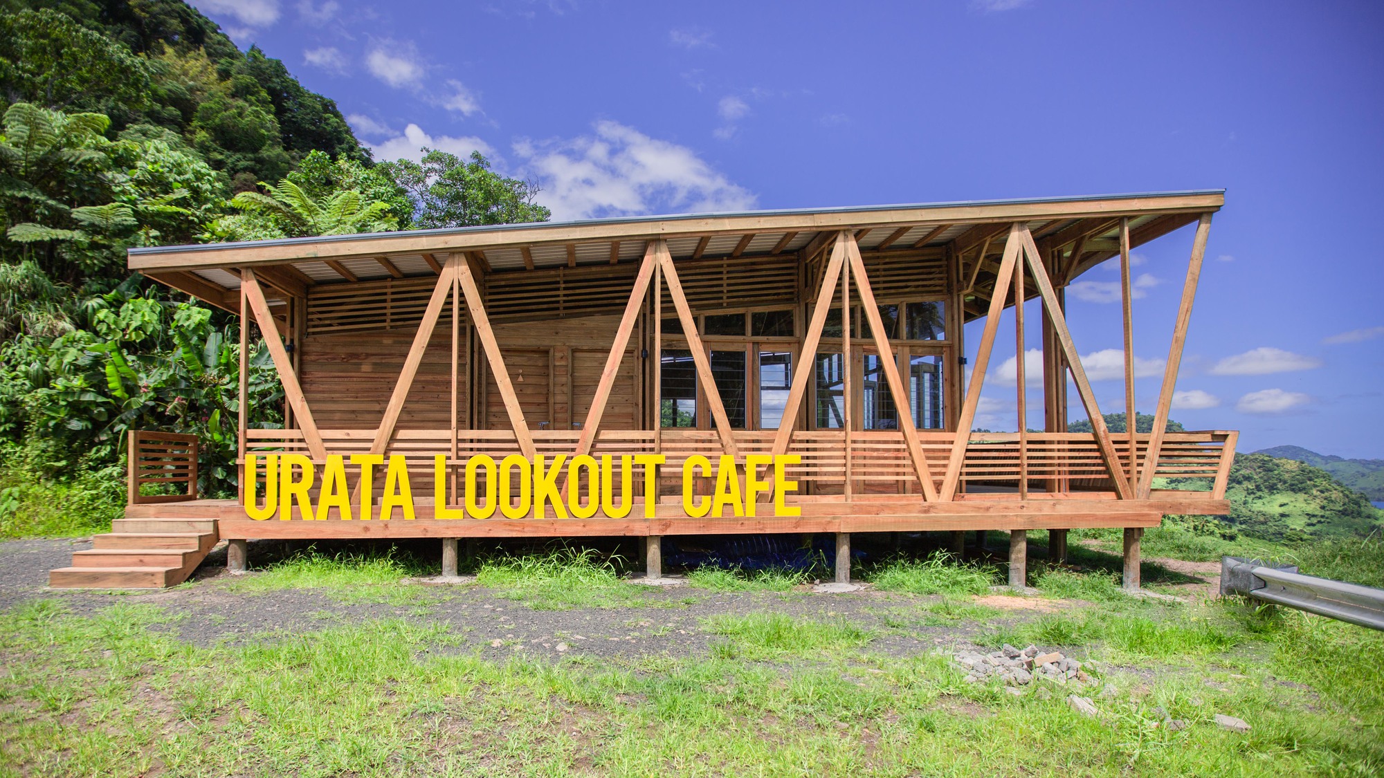 Elevated timber pavilion with A-frame diagonal bracing and horizontal slatted screens on a grassy hillside