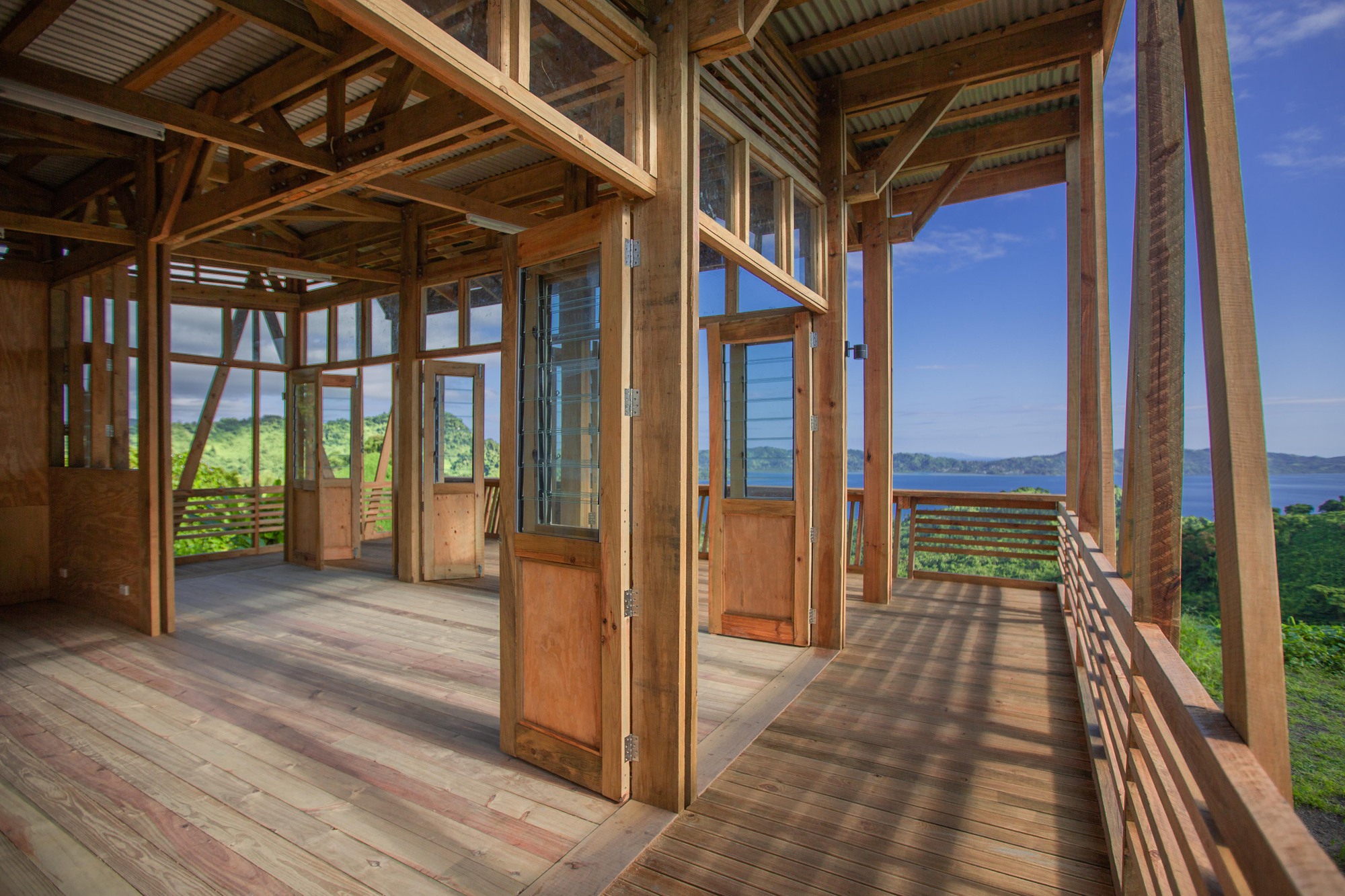 Interior of the timber pavilion with exposed diagonal bracing, glazed doors and ocean views beyond