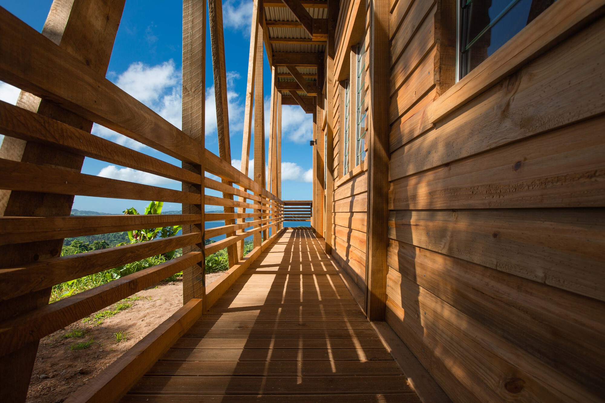 Narrow exterior walkway with horizontal timber railings casting afternoon shadows on the deck