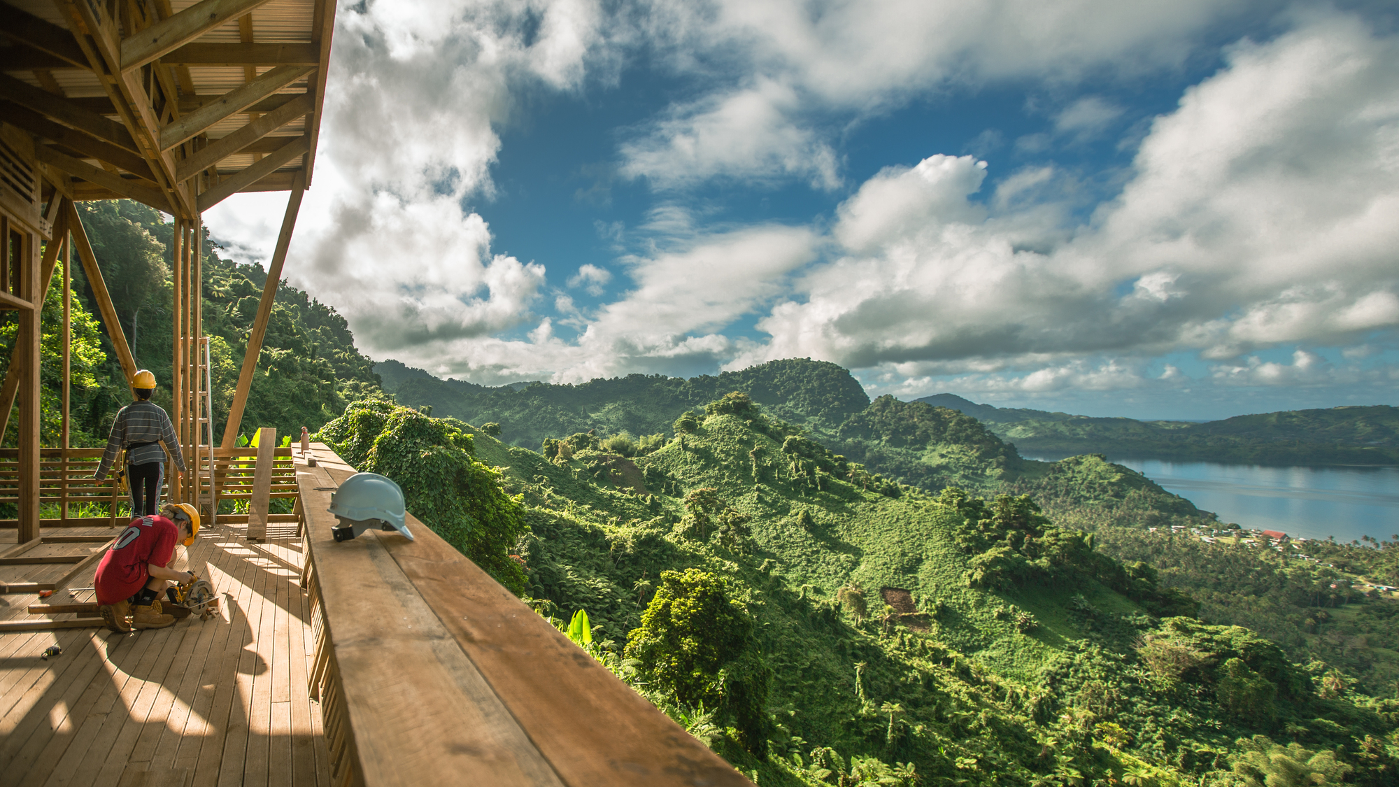 Covered deck with workbench overlooking forested hills and a lake under scattered clouds