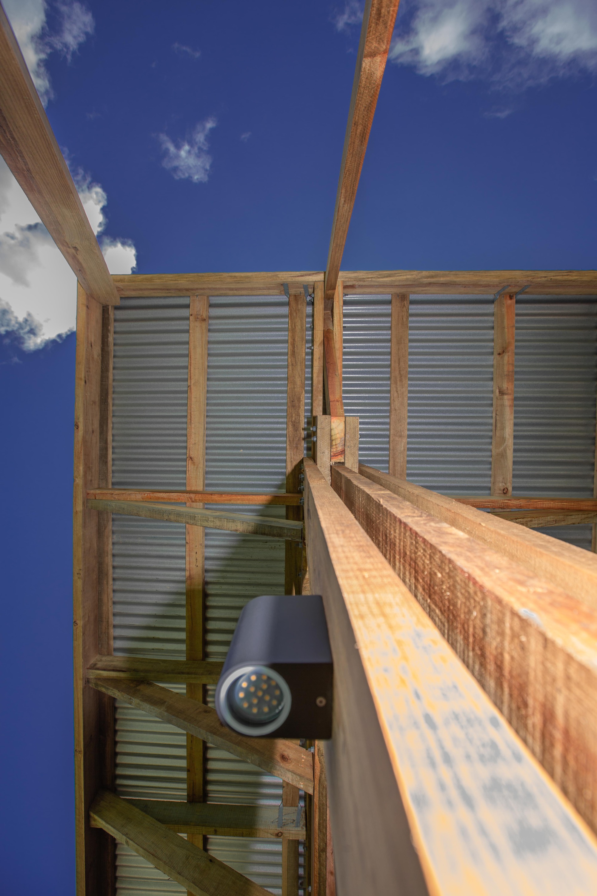 Upward view of timber beams meeting corrugated metal panels with an open sky beyond