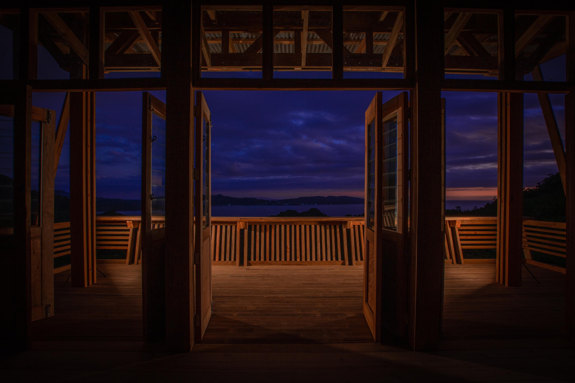 Interior view through timber frame and glass doors to the deck railing at dusk