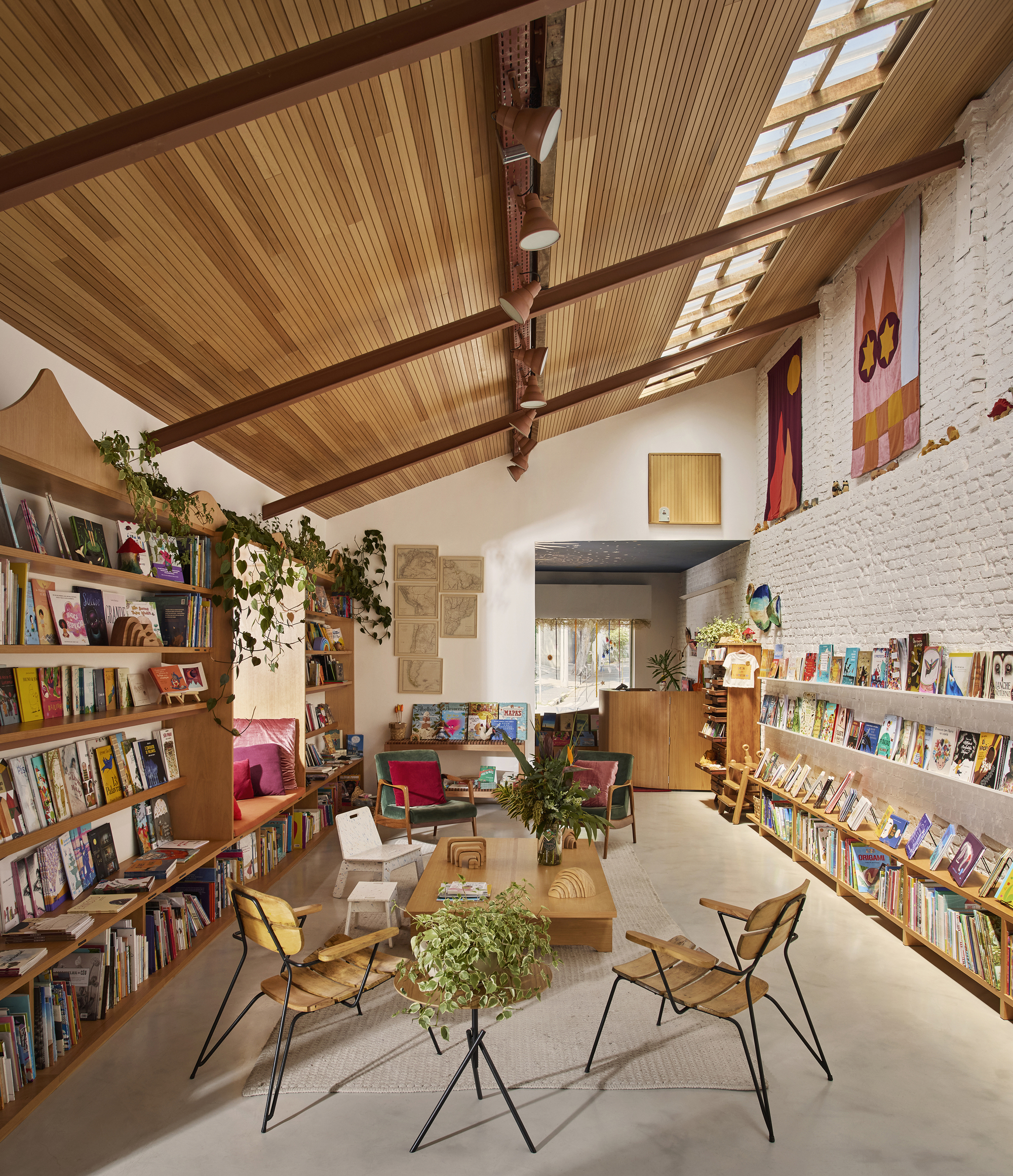 Interior of a bookshop with timber-slatted ceiling, exposed beams, skylights and trailing vines
