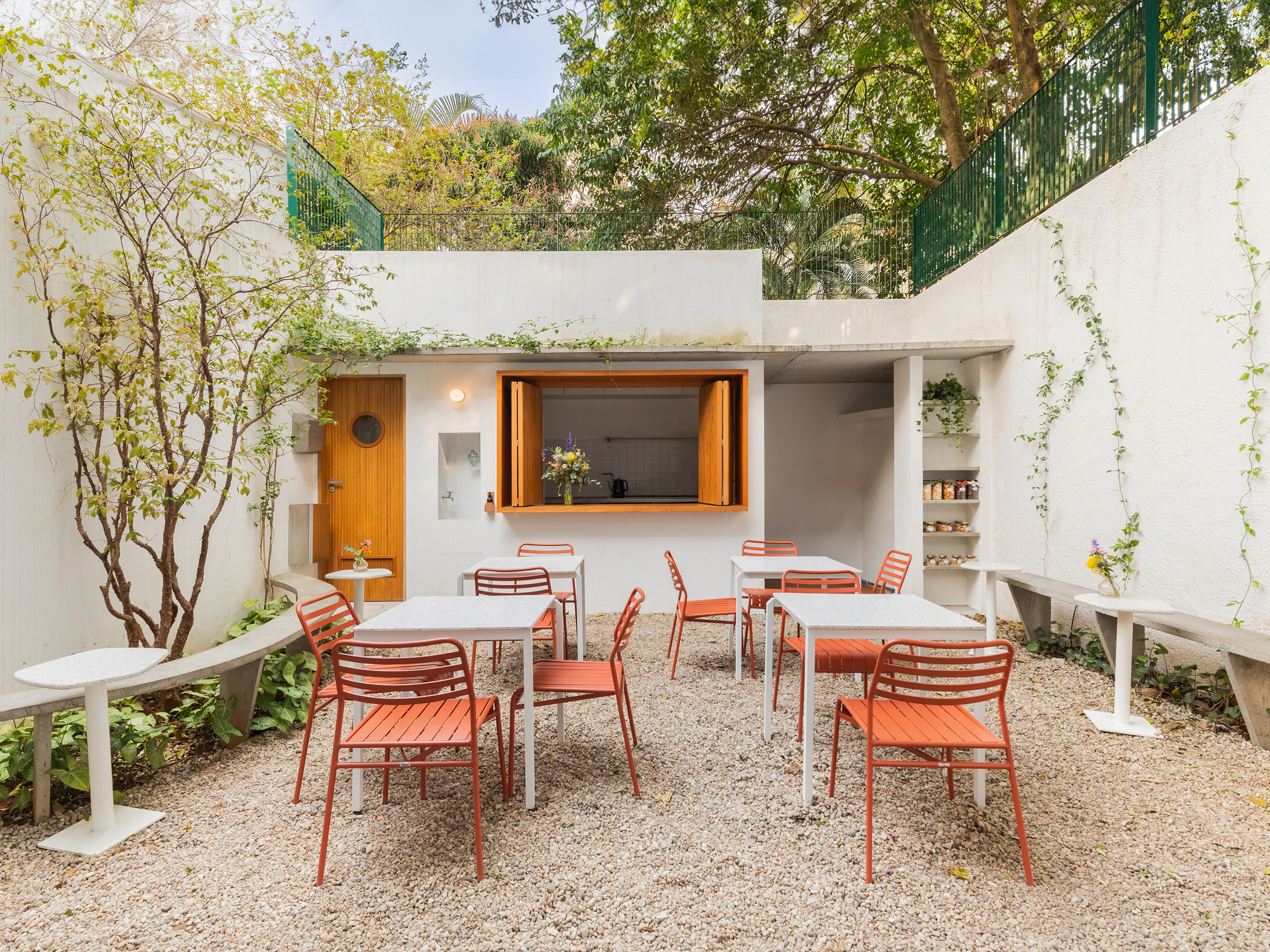 Outdoor courtyard with gravel flooring, coral chairs, timber service window and planted tree
