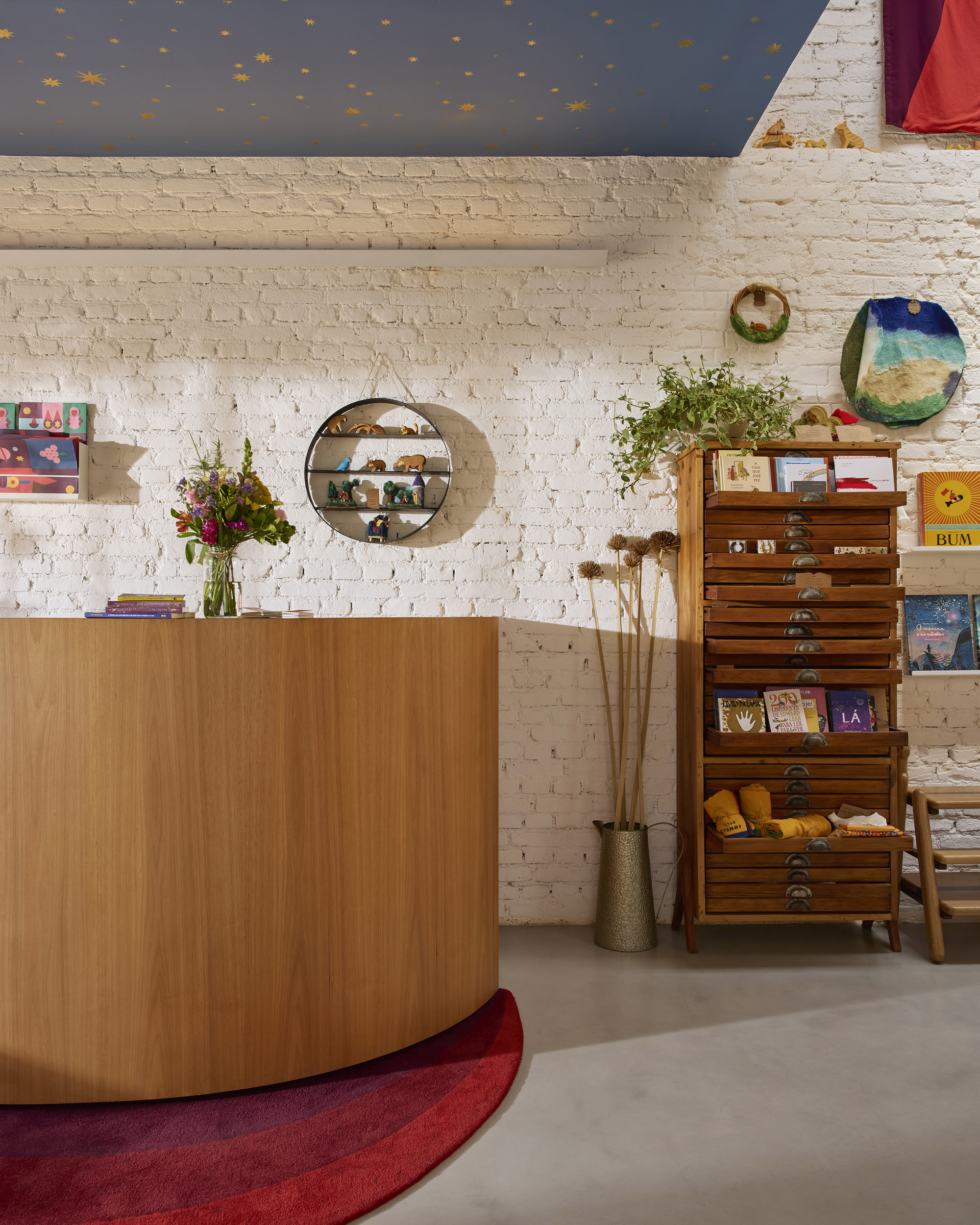 Interior view of curved timber service desk against whitewashed brick wall with round mirror and painted blue ceiling