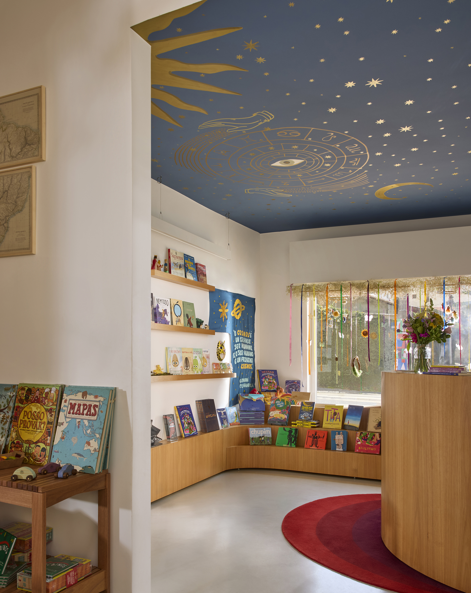 Curved timber display shelving beneath hand-painted celestial ceiling mural with sun, moon, and stars in blue and gold