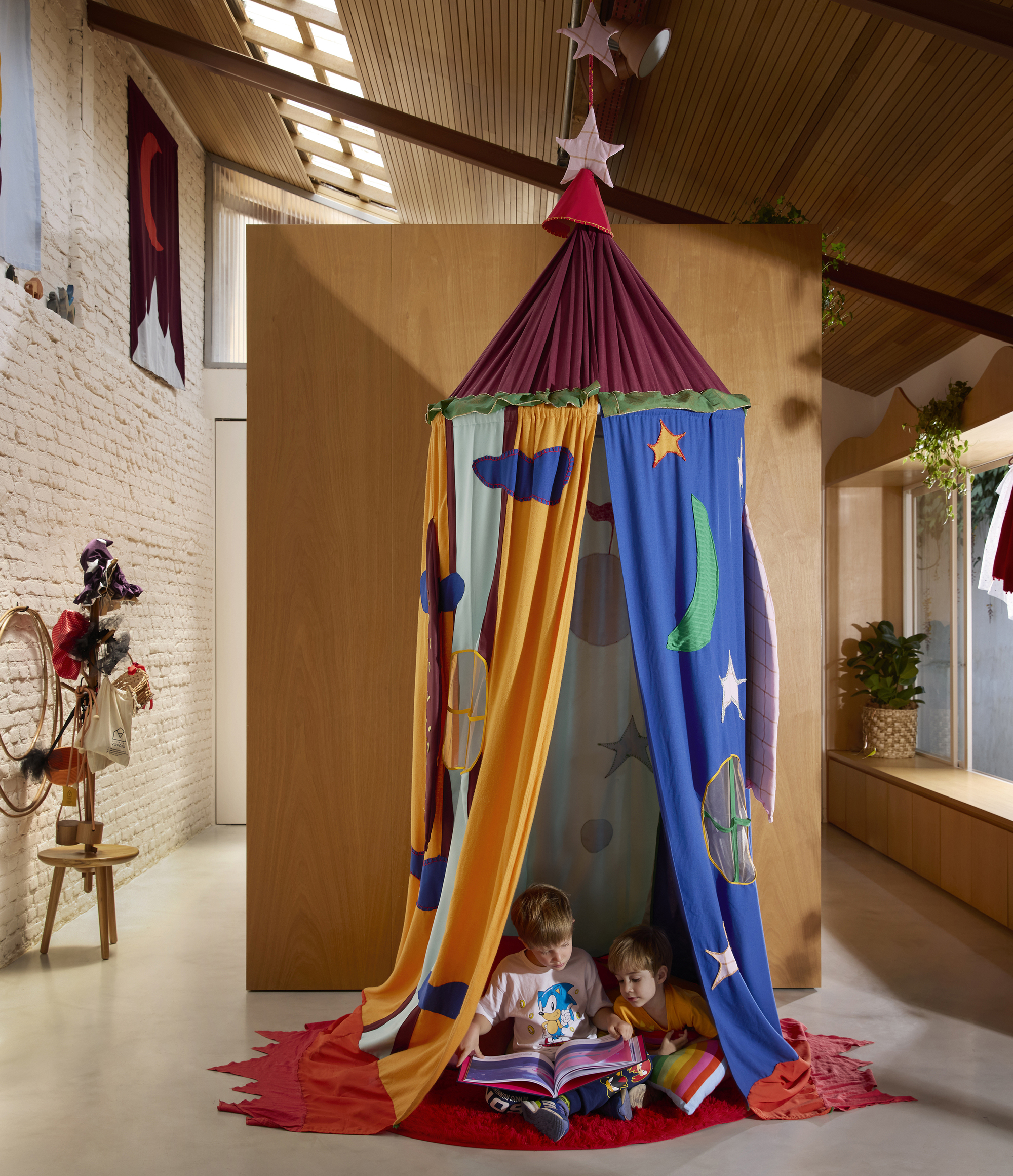 Fabric play tent with celestial appliqués in double-height space with slatted timber ceiling and whitewashed brick wall