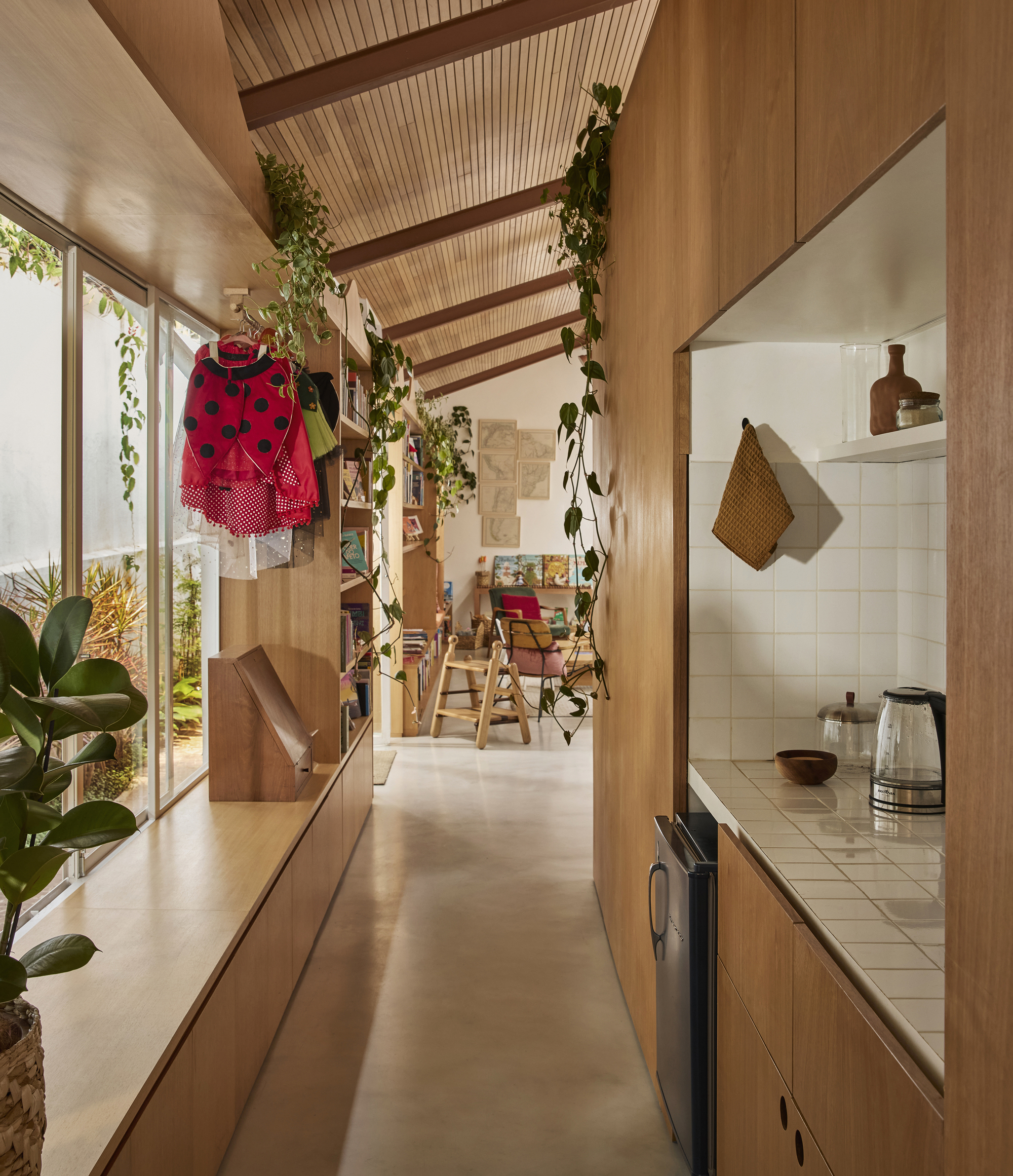 Galley corridor with timber slat ceiling and hanging plants leading toward kitchen with white tile