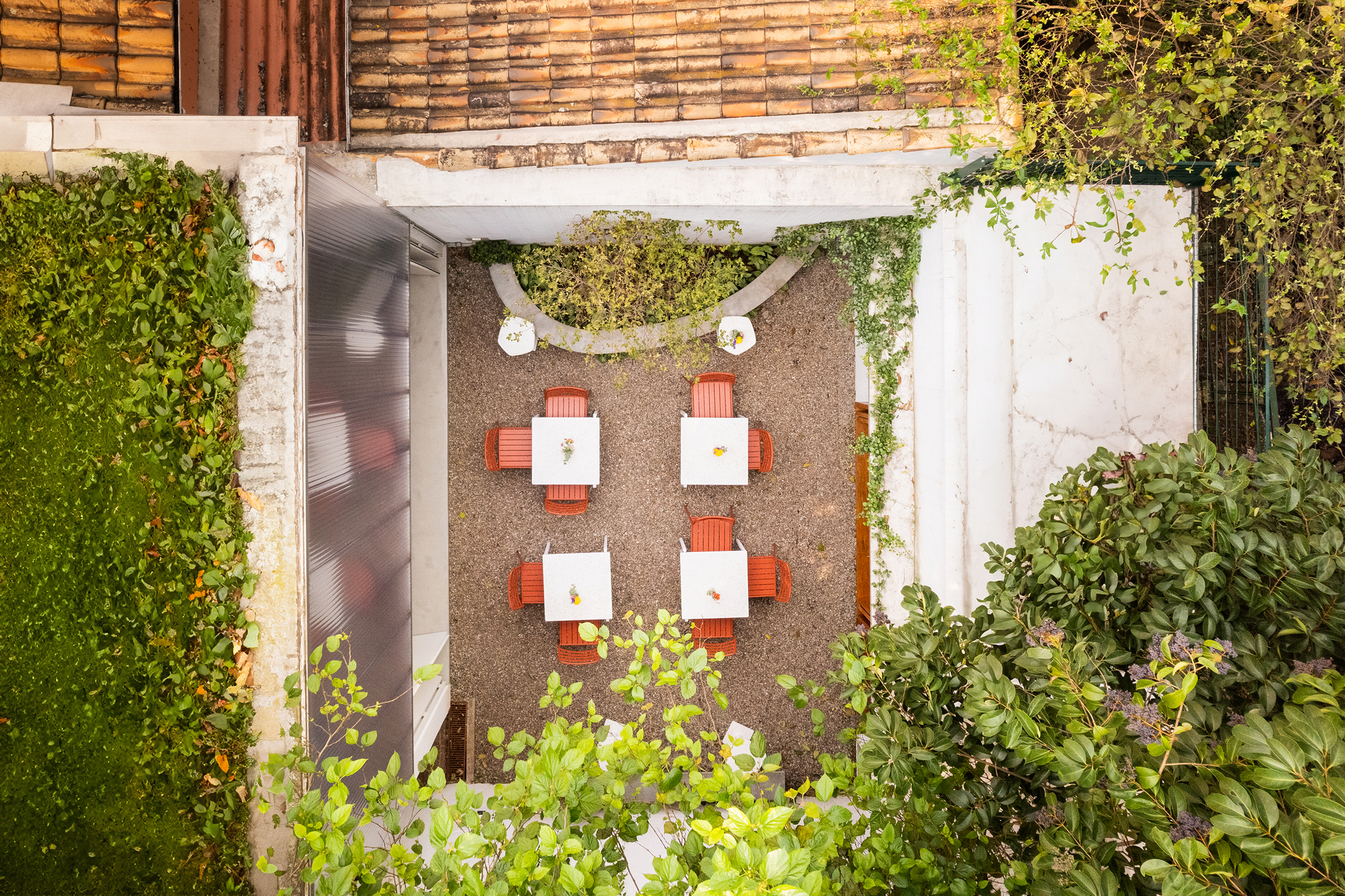 Overhead view of gravel courtyard with orange dining chairs and curved planted bed with white bench