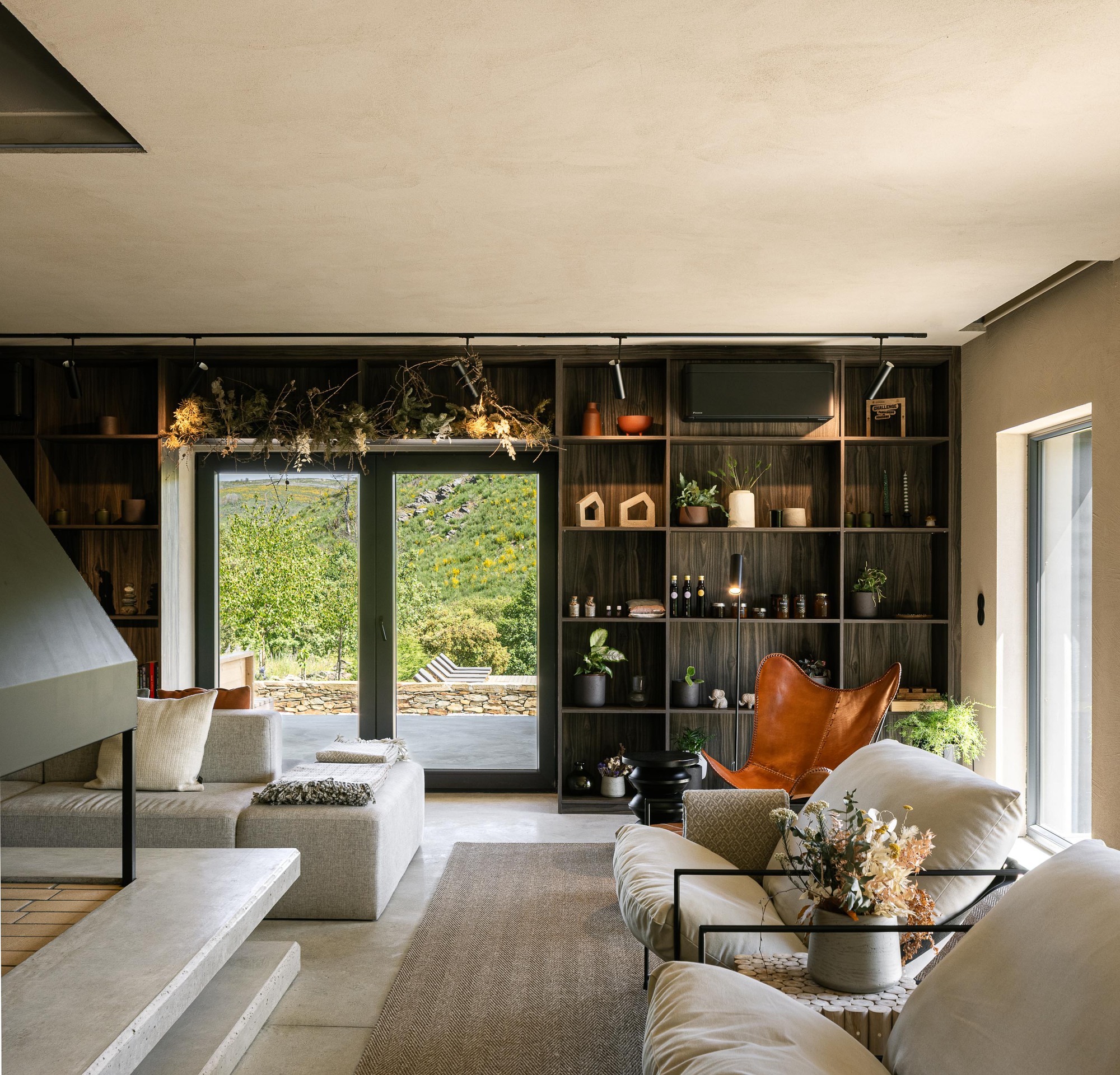 Living space with dark timber shelving wall and glazed doors opening to a stone terrace outside