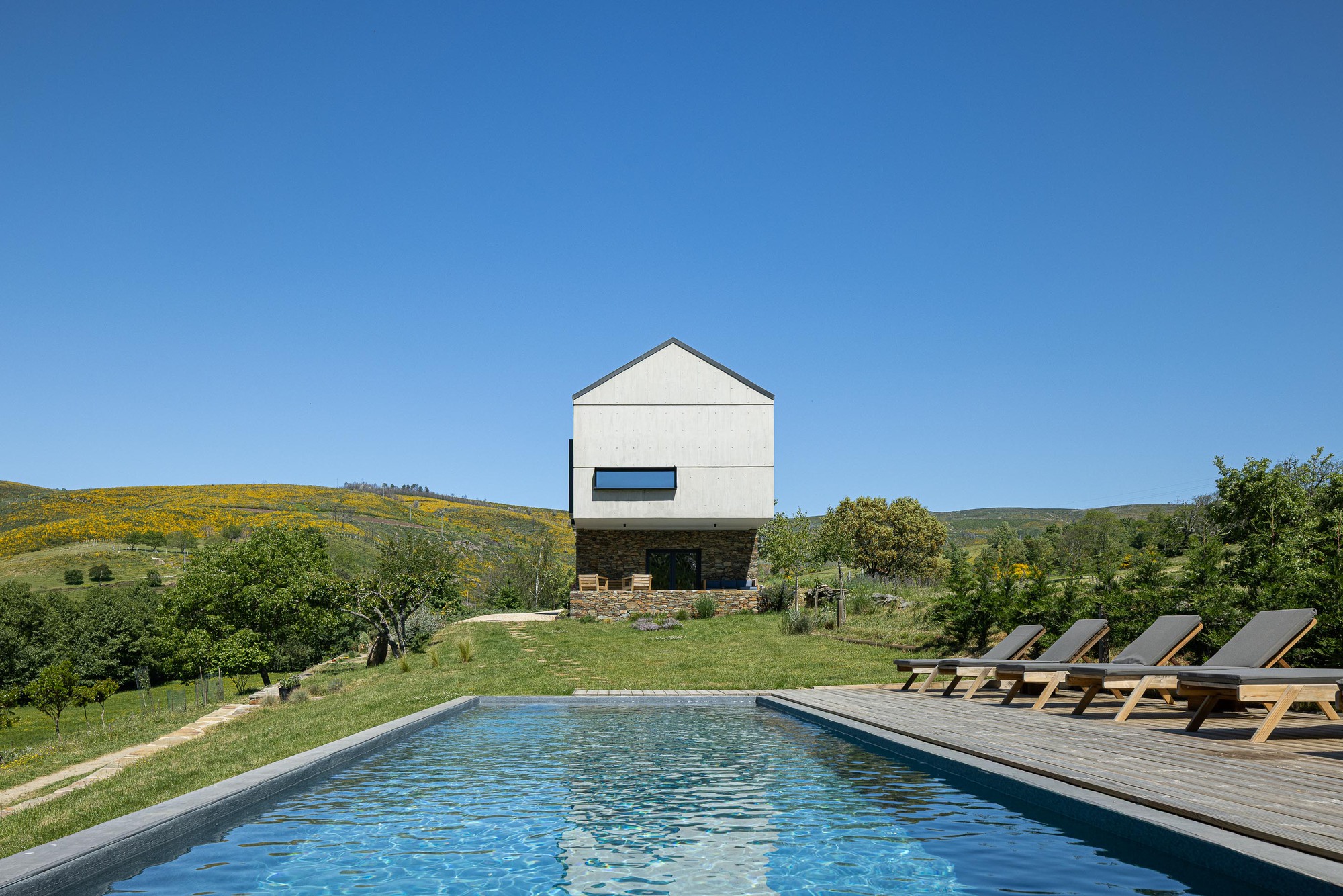 White rendered volume elevated on stone base beside swimming pool with timber deck and loungers