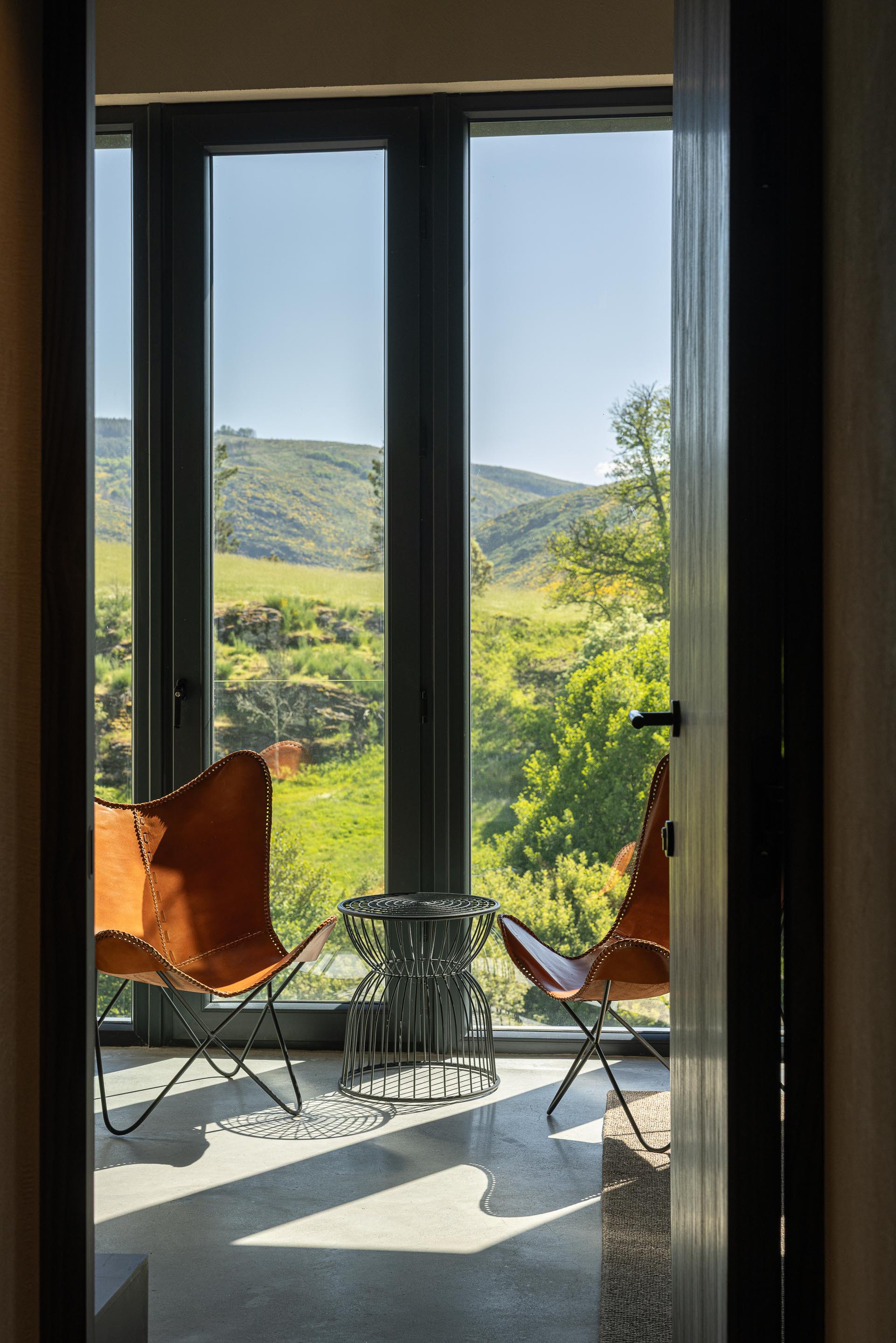 Glass doors opening from interior to a terrace with leather butterfly chairs overlooking green valley hillsides