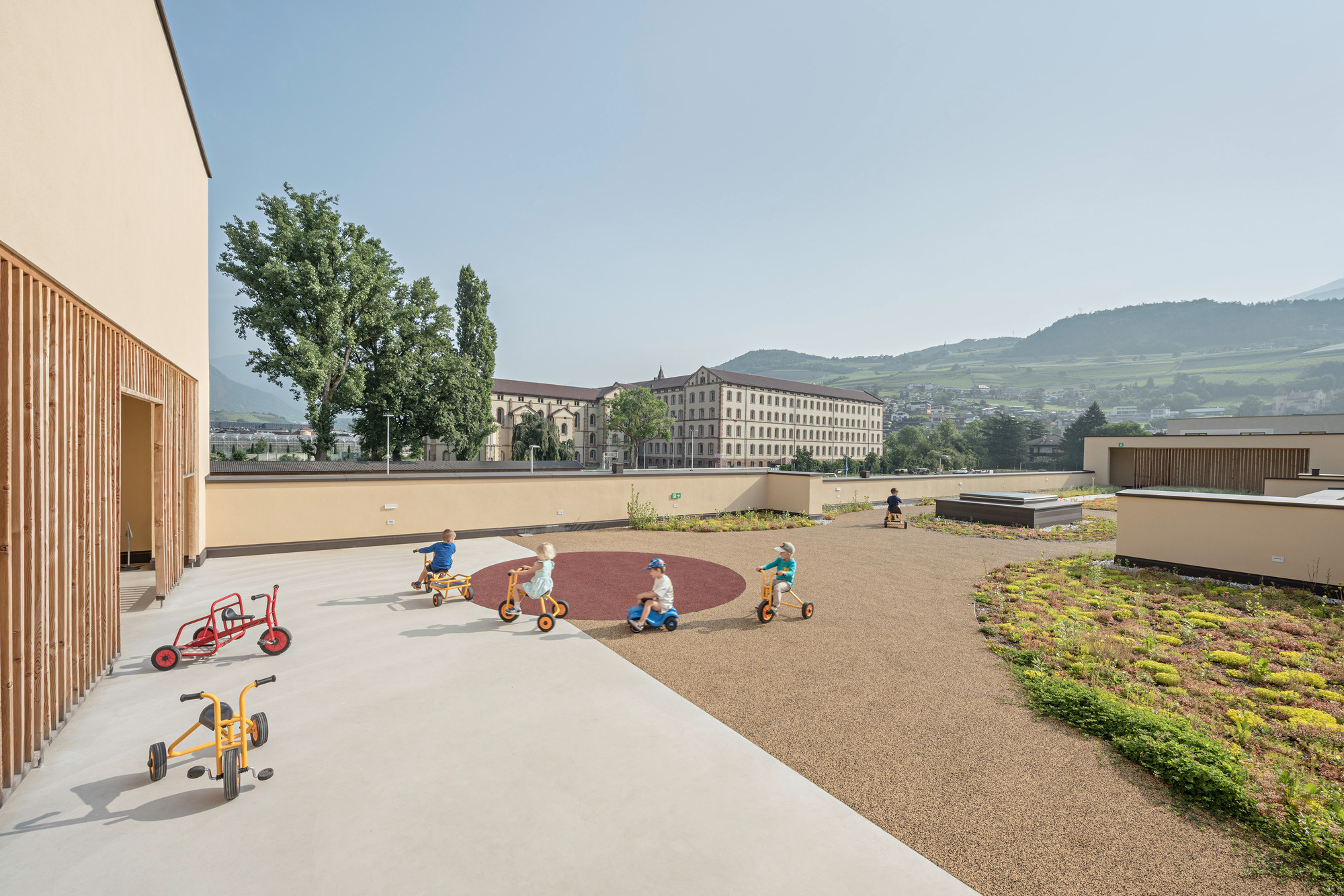 Rooftop play terrace with circular path and sedum green roof under distant hills