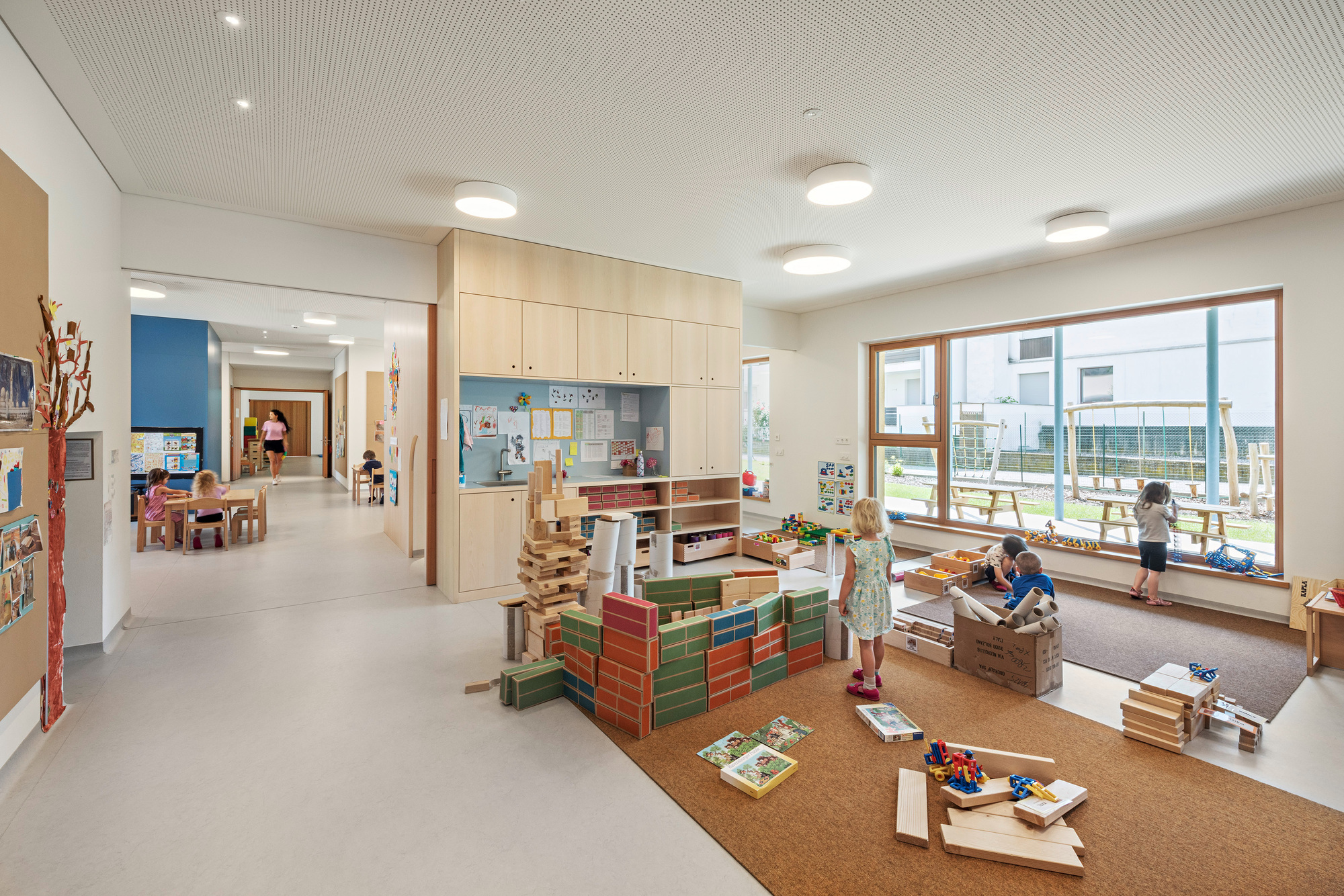 Interior classroom with cork flooring and children building with wooden blocks near a window seat
