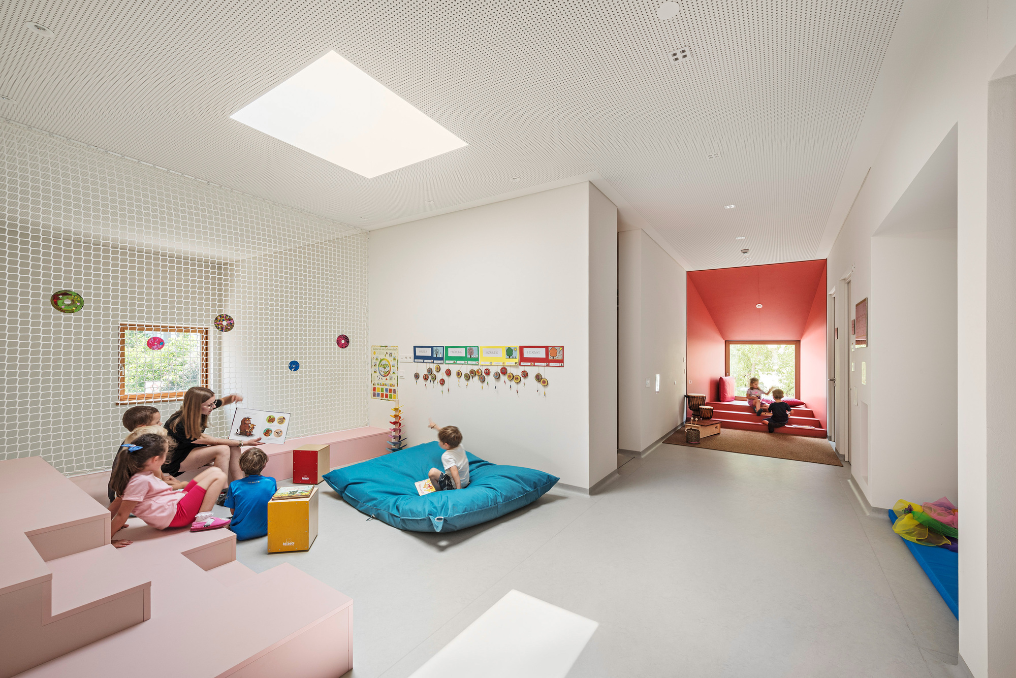 Learning space with perforated wall panel and red alcove window seat visible through open doorway