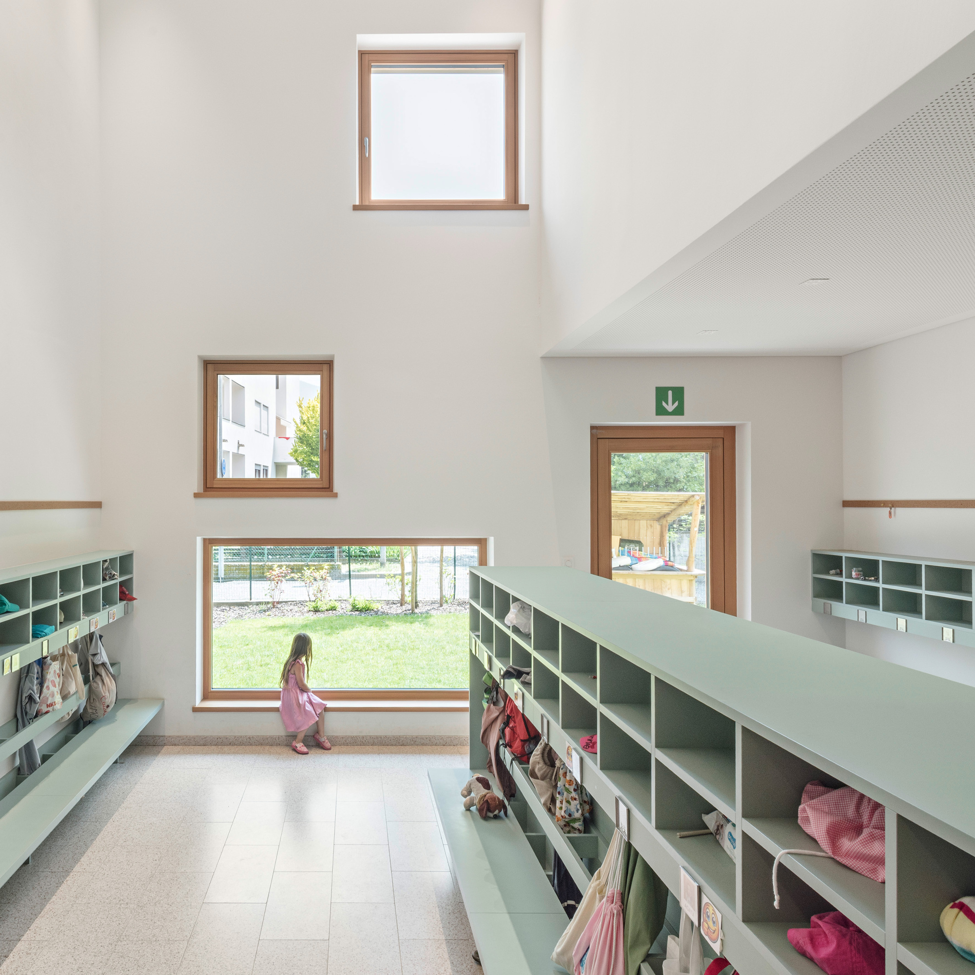 Double-height entrance hall with green storage cubbies and child walking past horizontal window