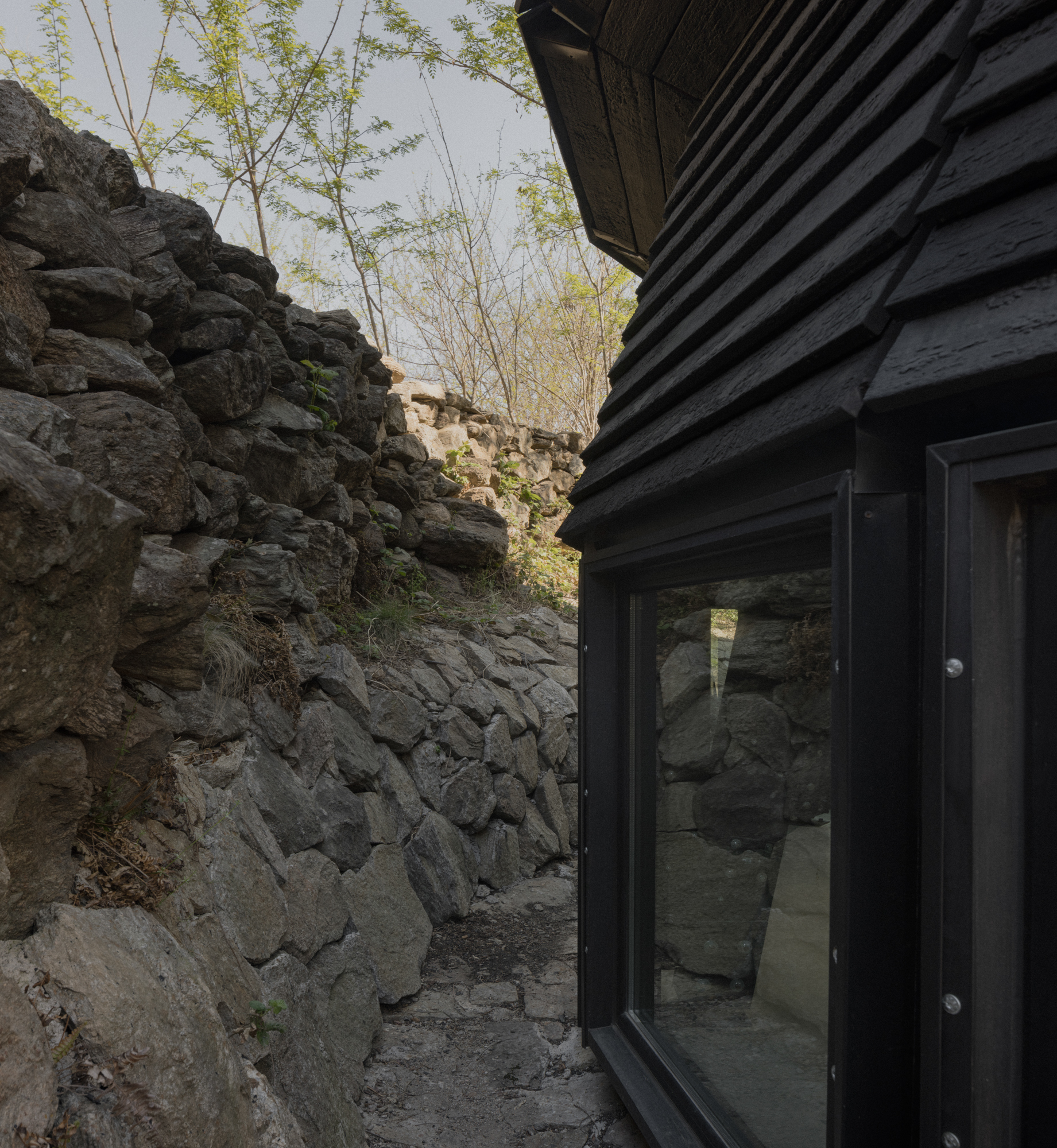 Glass door in blackened wood facade opening onto a narrow courtyard carved from volcanic rock