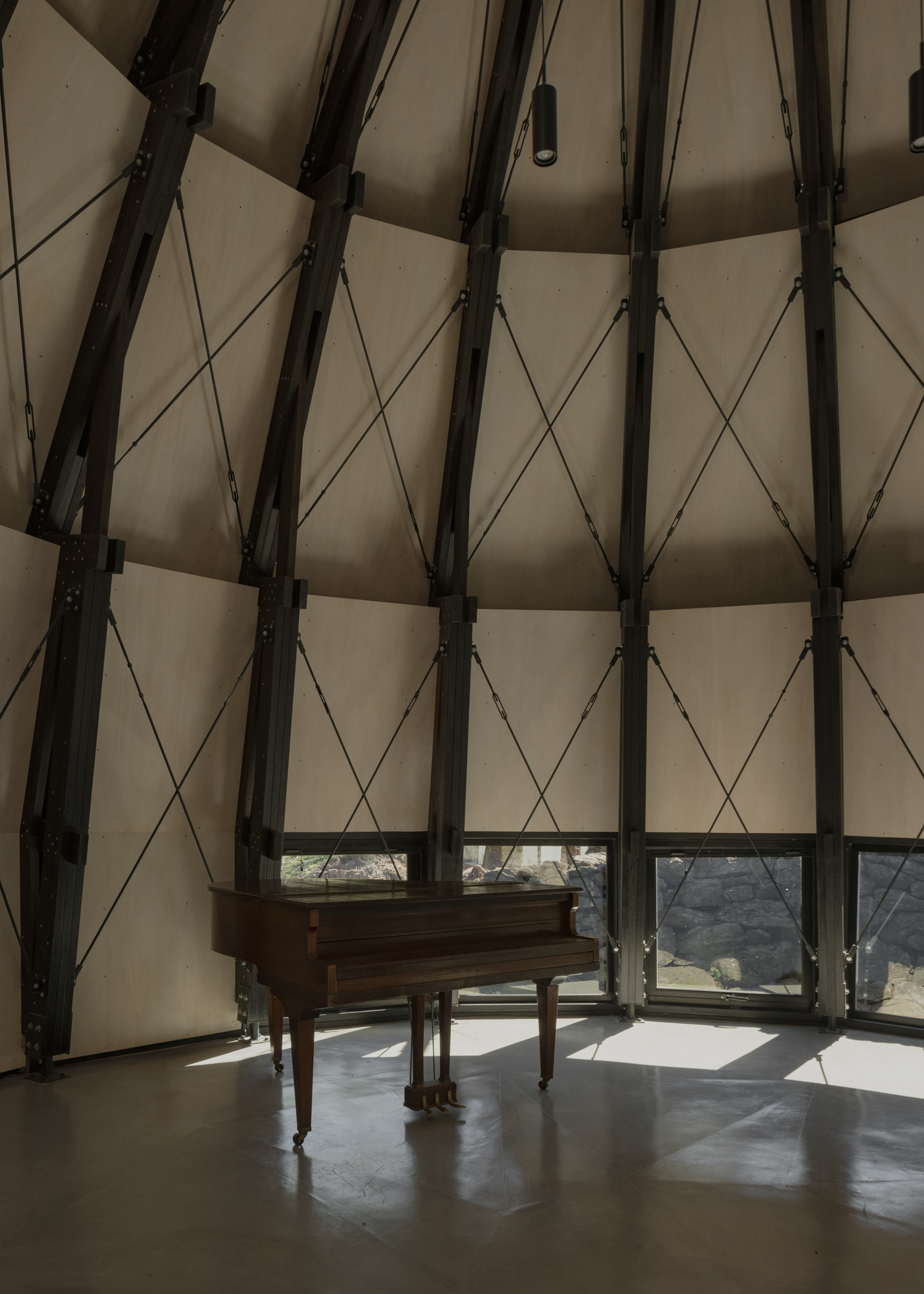 Interior of the conical volume with exposed steel beams, cable bracing and a piano on polished concrete
