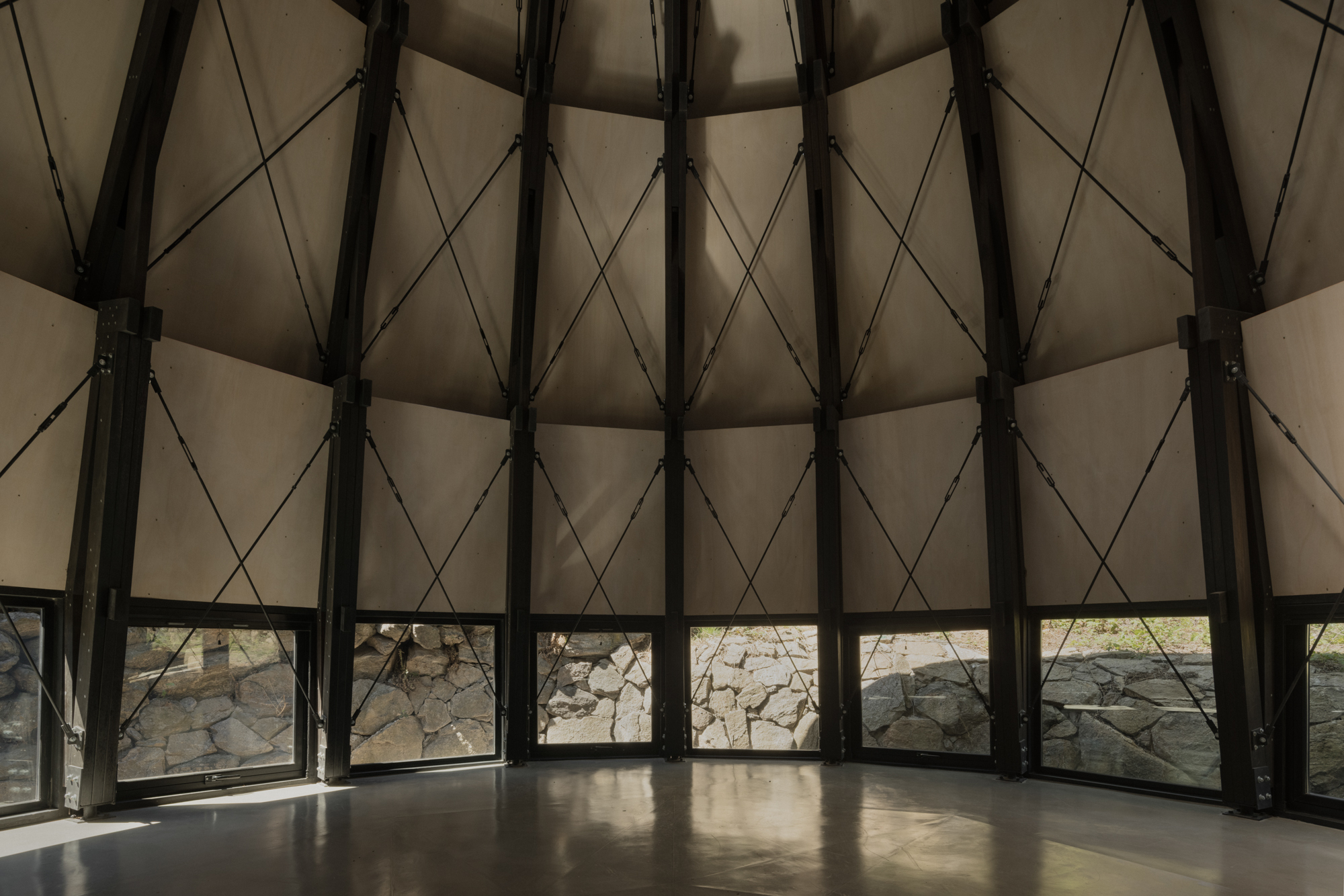 Radial steel structure with diagonal cable tensioning and ribbon windows overlooking the rocky landscape