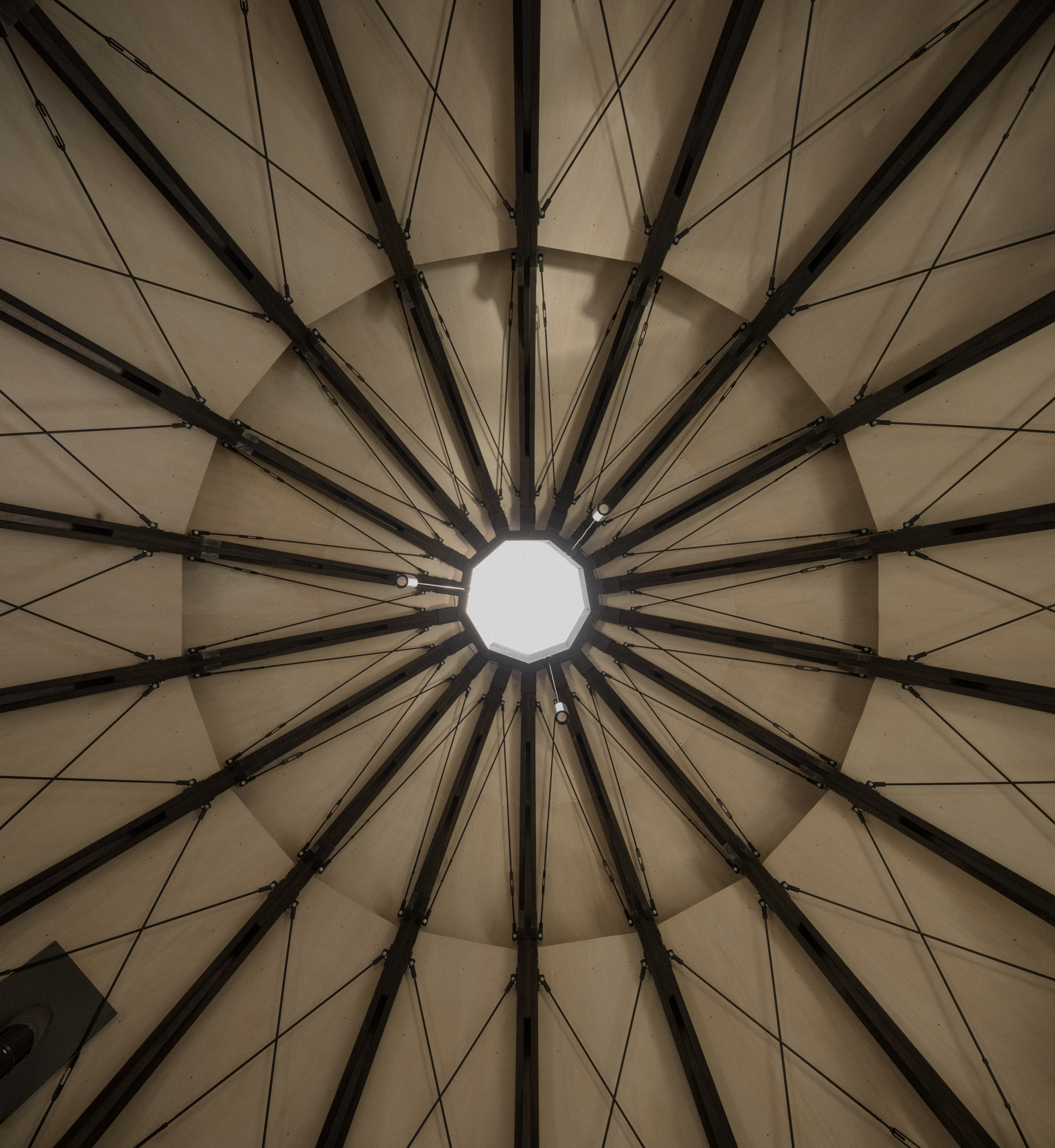 Looking up at the conical ceiling with radiating steel beams meeting at a circular skylight