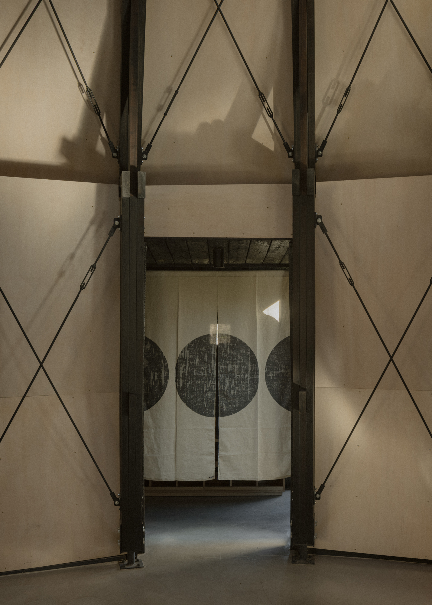 Interior view through structural bays toward a hanging textile with circular motifs in the adjacent room
