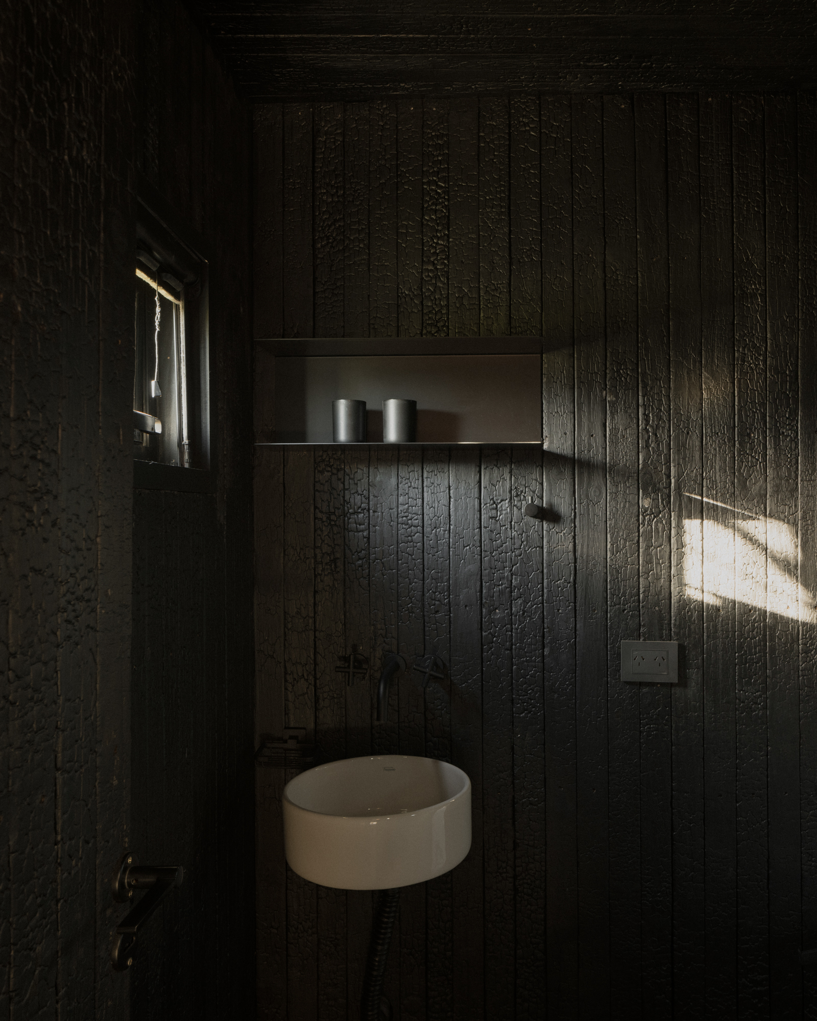 Small powder room with charred timber wall cladding and a round basin under a narrow shelf