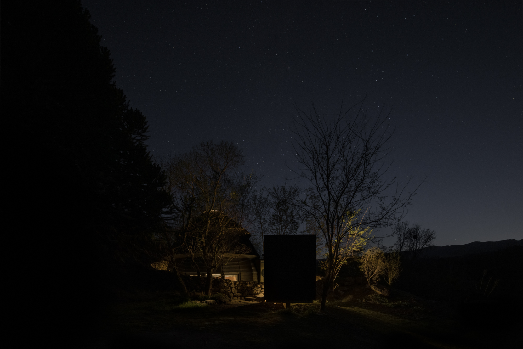 Night view of illuminated dome and timber box volumes under a star-filled sky