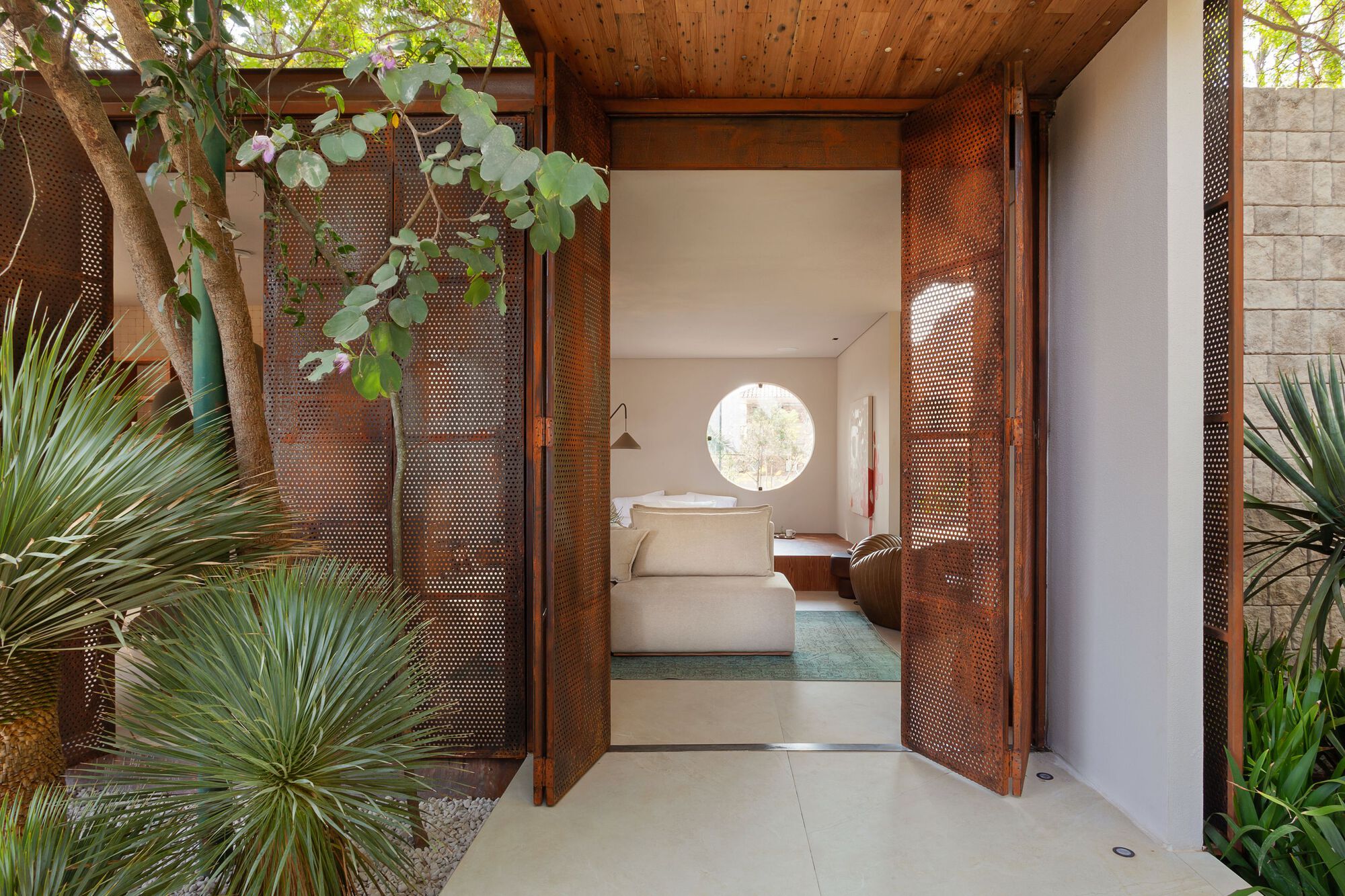 Open perforated metal doors framing a view into a bedroom with circular window and climbing vines